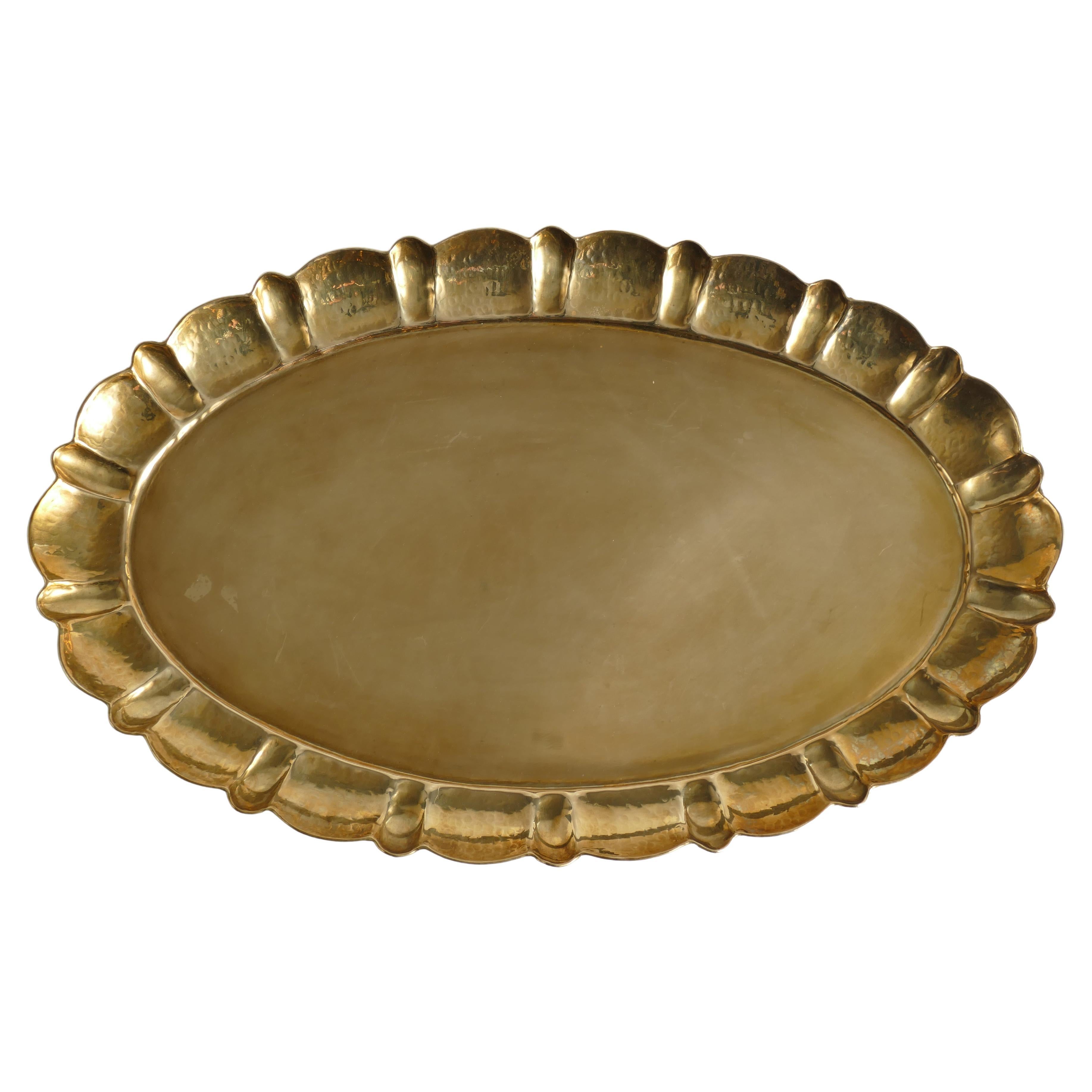 Masterfully crafted brass tray featuring an oval shape with a gracefully contoured, hand-hammered edge. Manual operation and stamped for authenticity. The hammered decor and profiled edge enhance its unique charm. This exquisite tray, designed by