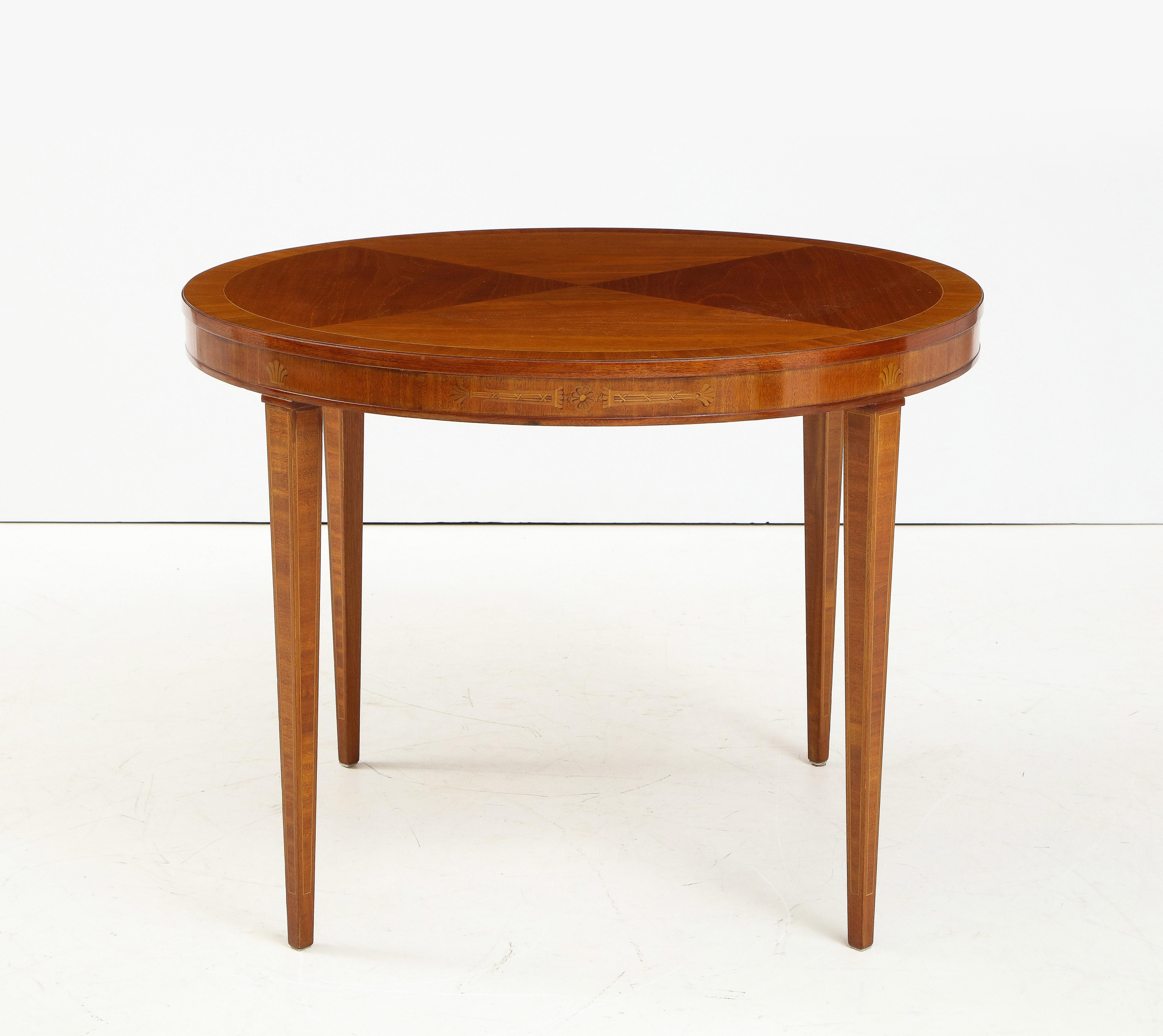 A Swedish Grace fruitwood inlaid mahogany table, Circa 1940s, the circular top with four pie shaped veneers and a cross banded edge. The frieze with classical inspired fruitwood inlays, raised on square tapered legs.

 