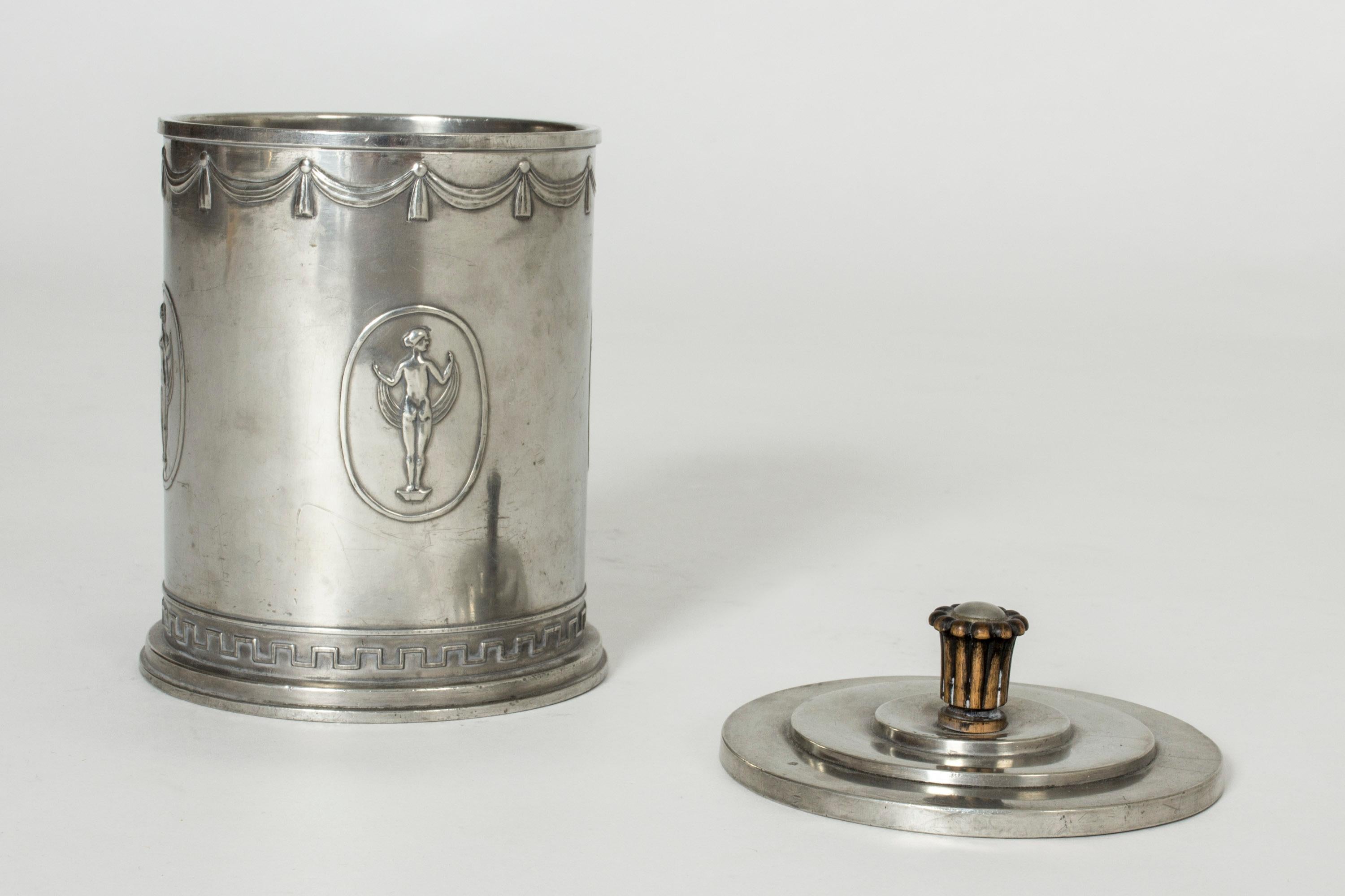 Rare, elegant pewter jar from the Swedish Grace period, made by Schreuder & Olsson. Decor of woman in different poses around the body and a Classic meandering pattern around the base. Sculpted wooden knob on the lid.