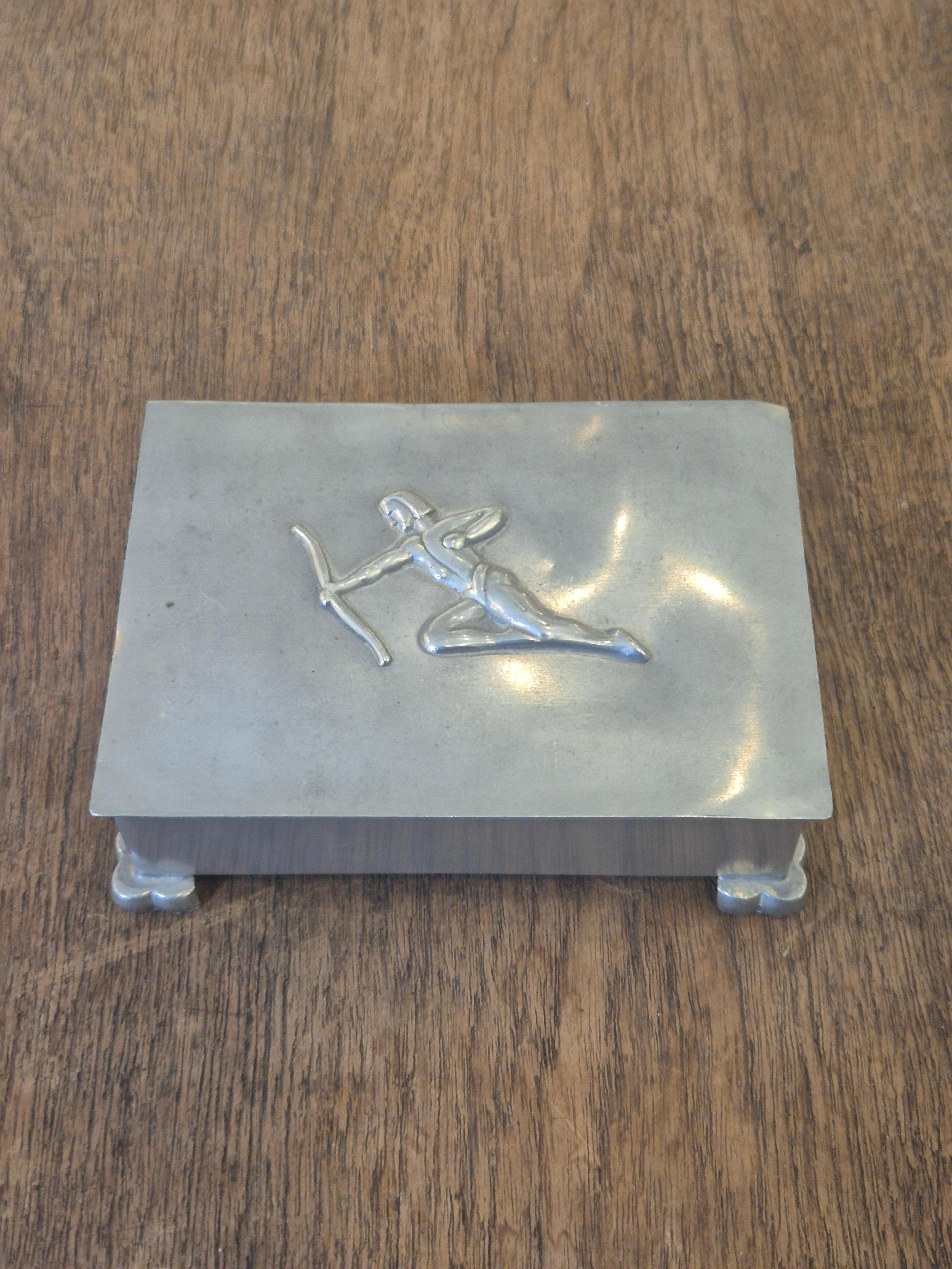 Eine dekorative und funktionelle Deckelbox, ideal für Schmuck, Zigaretten oder zum Verstecken kleinerer Gegenstände. Dekor des Bogenschützen. 

Mit Punzierung Sv.M, L8 = 1937. Schwedische Gnade. 