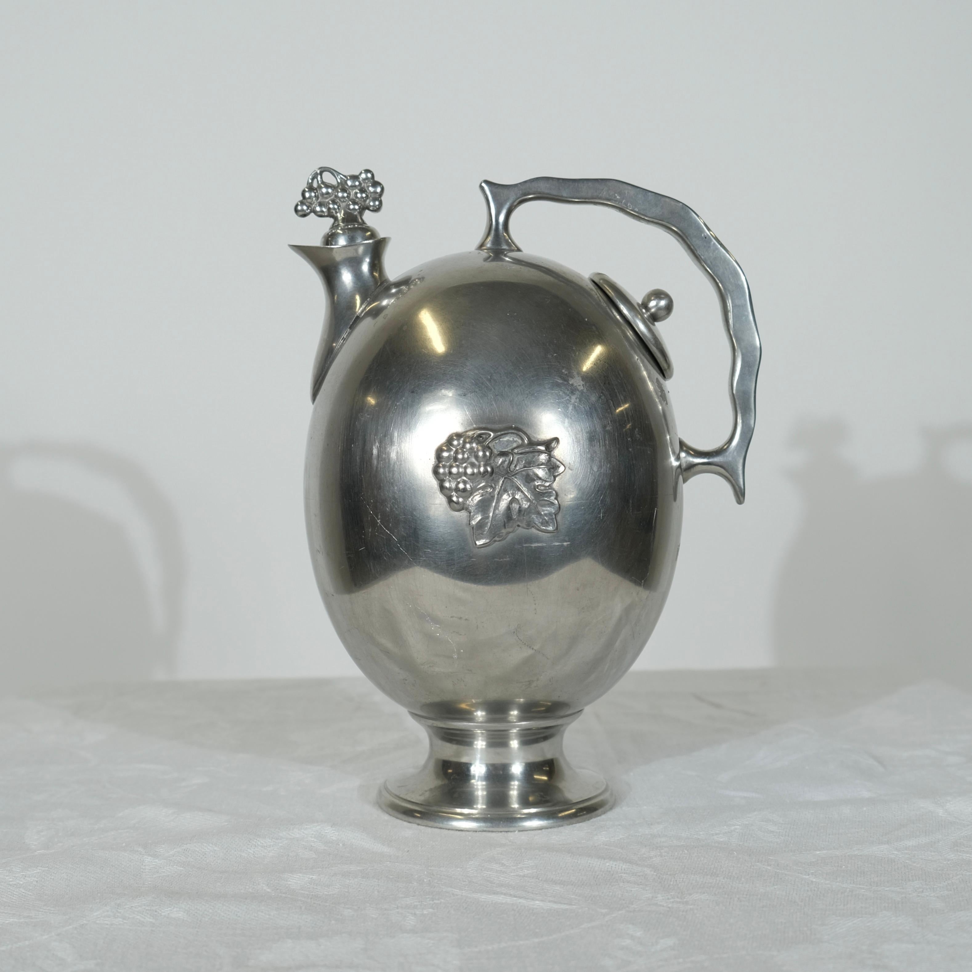Exquise cruche à vin en étain Swedish Grace de 1933. Cet élégant pichet à vin en étain, fabriqué en 1933 pendant la période de grâce suédoise, incarne un mélange raffiné de classicisme et de modernité. La cruche présente un corps ovale remarquable