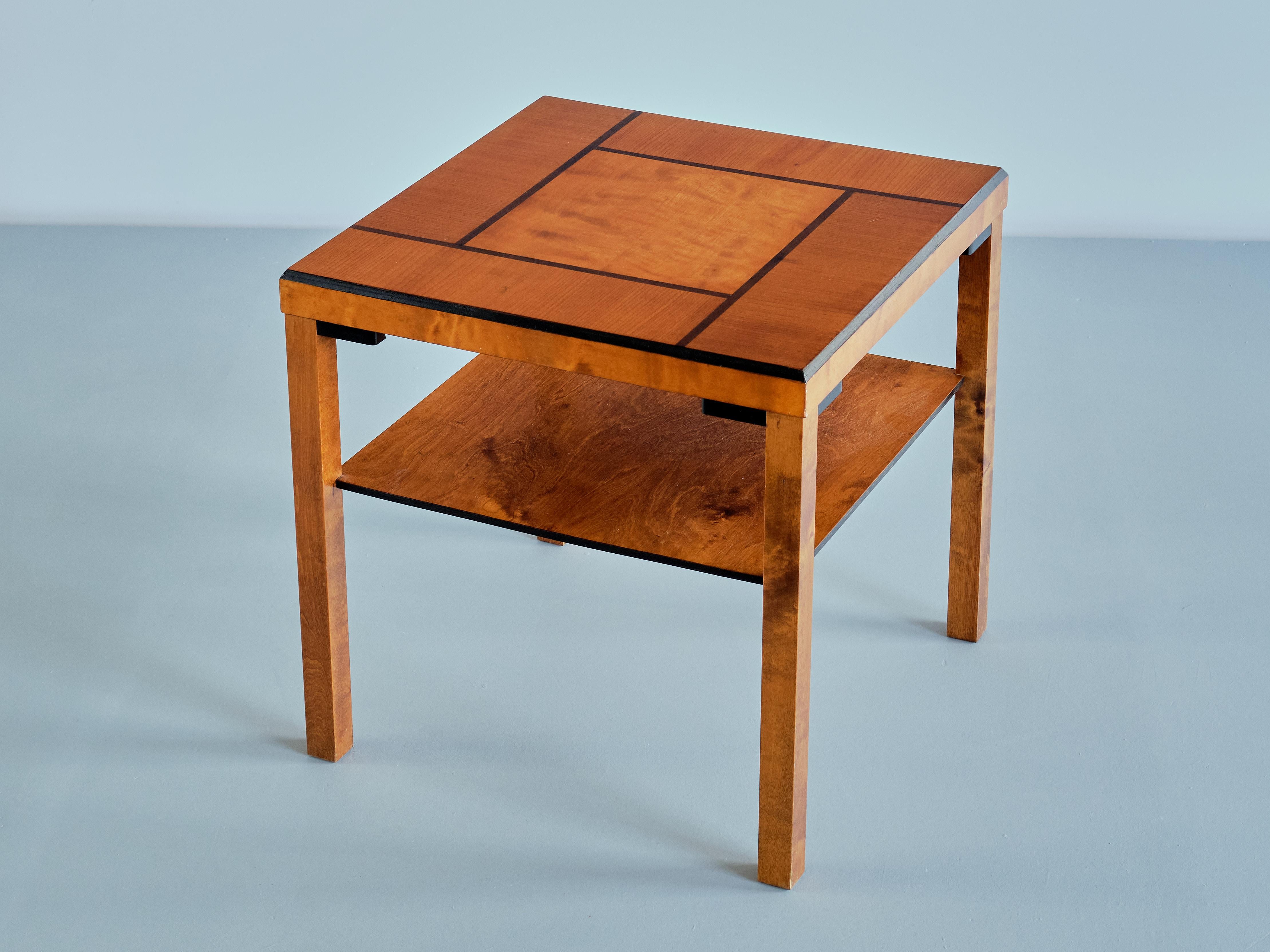 Cette élégante table d'appoint/café a été produite en Suède dans les années 1930. Le design est marqué par la forme carrée du plateau et des pieds. Le plateau est plaqué en orme et en bouleau, avec un carré central flanqué de barres rectangulaires.