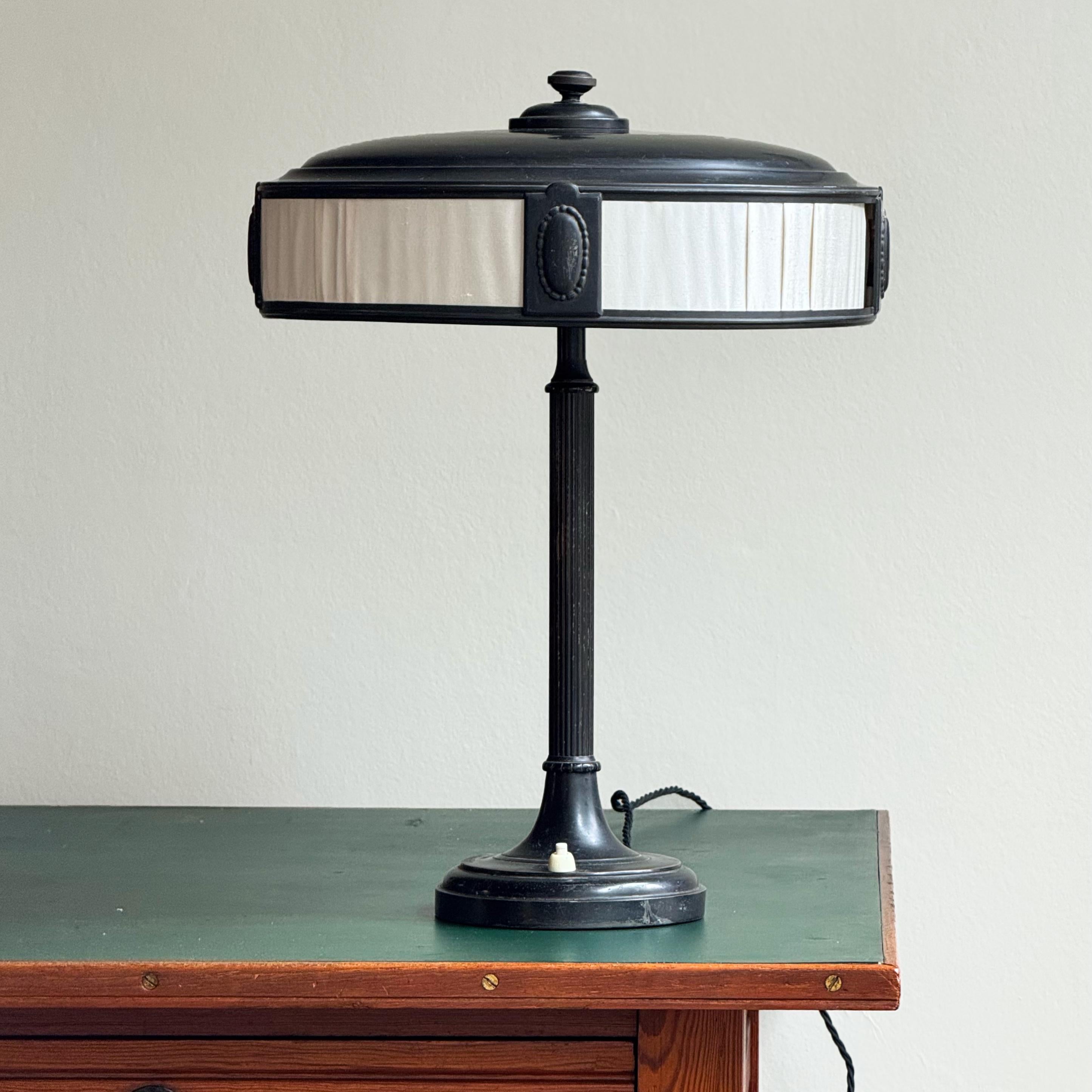 Description:

An elegant Swedish table lamp with blackened brass frame and silk screen. With classical motifs throughout, from its columnar base to repeated roundel motifs, this lamp is emblematic of the persistence of neo-classicism in Swedish