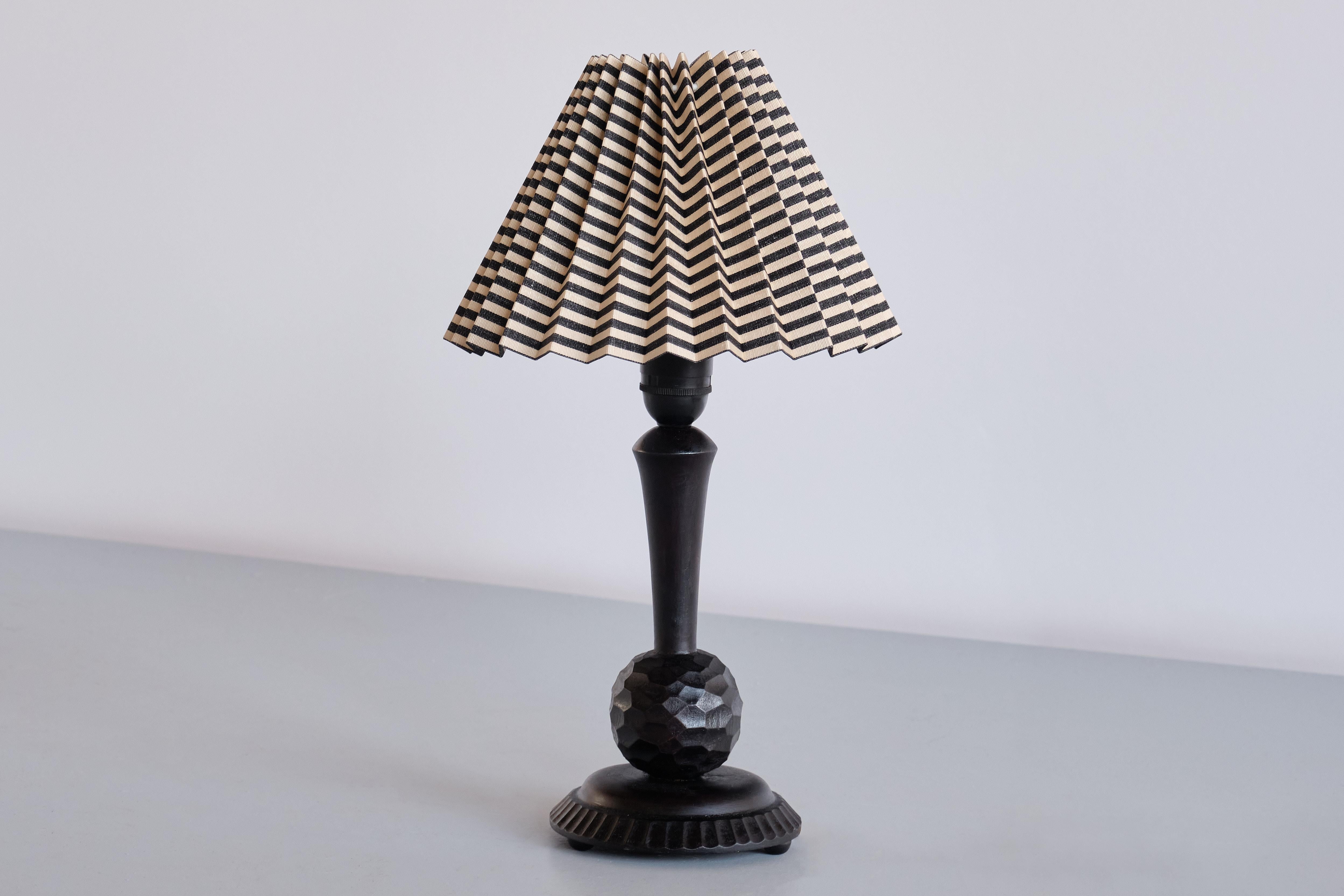This elegant table lamp was hand made in Sweden in the early 1930s.
The design is marked by the base in black lacquered birch wood. The sphere shape with intricate, hand carved details, giving the wood a beautiful texture. The circular base with