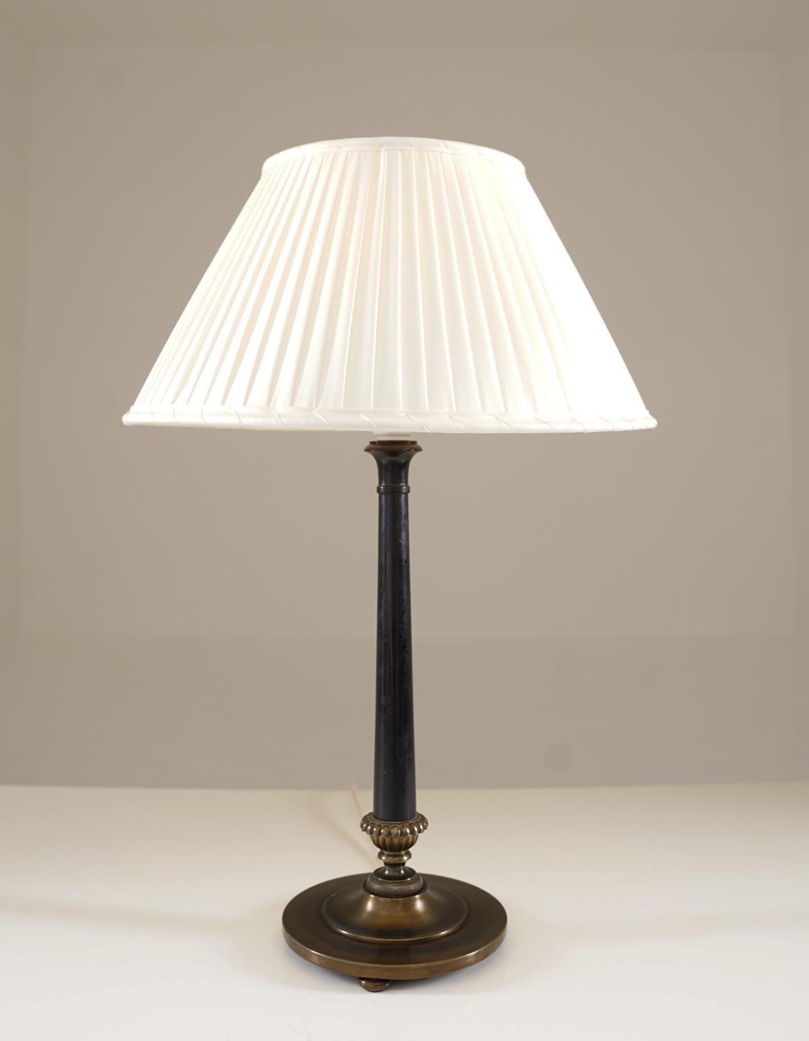 This elegant table lamp embodies the refined aesthetics of the Swedish Grace movement, crafted by the esteemed Nordiska Kompaniet during the 1920s. Its sophisticated design features a sleek black lacquered stem, gracefully tapered and complemented