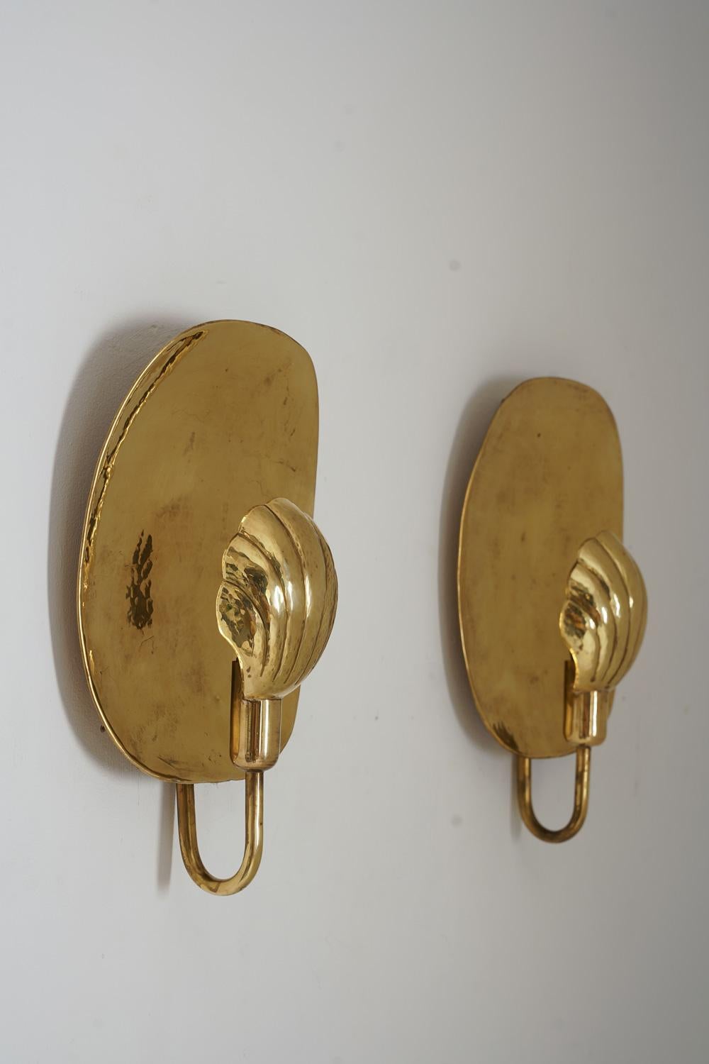 A pair of wall lights in brass by Lars Holsmtröm, Sweden.
Tha lamps consist of a hammered brass back plate and a light source (E-14), hidden by a sea shell-shaped reflector.
Lars Holmström is known as being one of the most skilled blacksmiths at the
