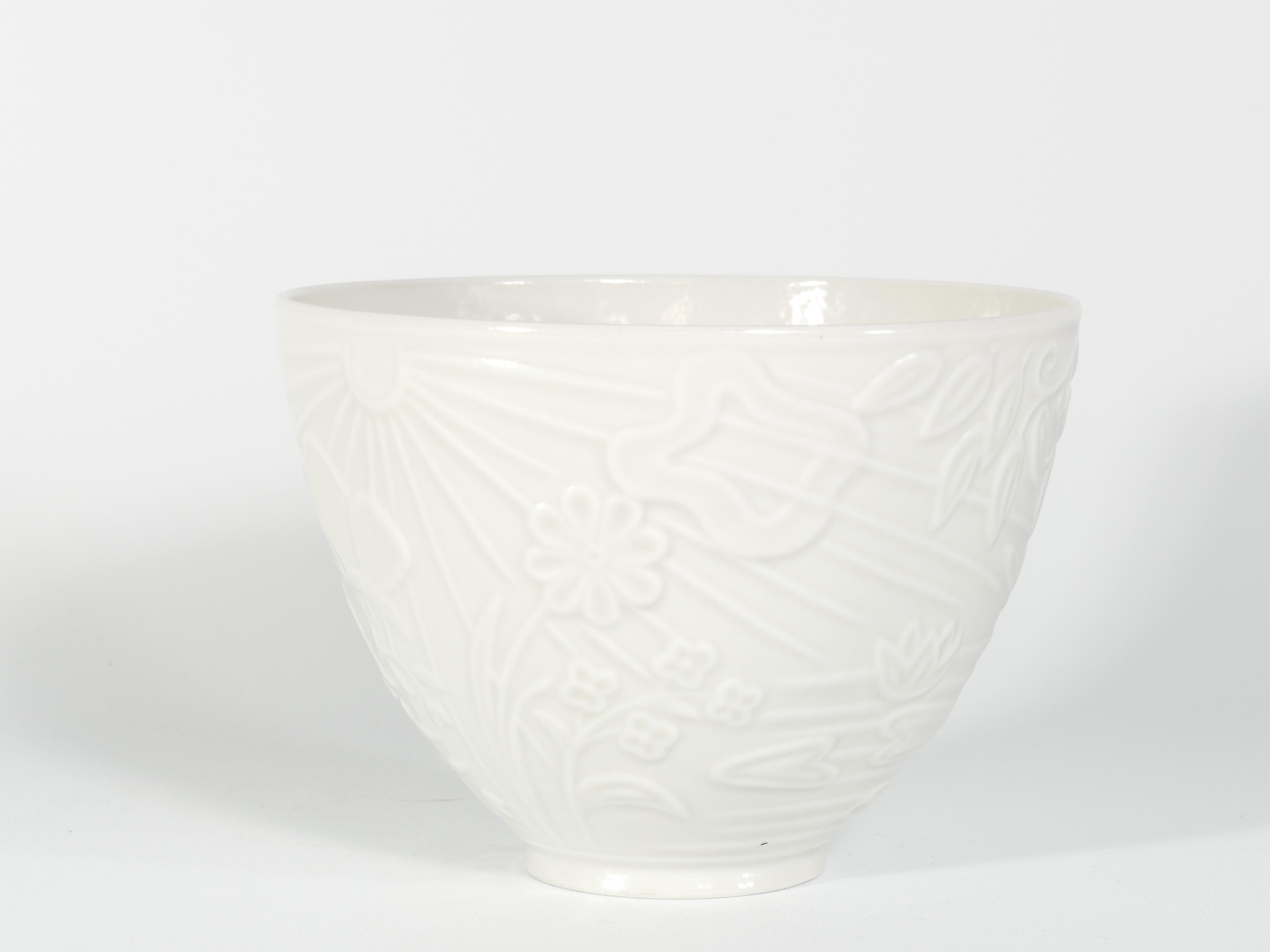 This is a thin, very rare, translucent white porcelain bowl designed by Gunnar Nylund for ALP Lidköping/Rörstrand. The bowl features a lovely relief decoration depicting the sun, clouds, water with waterlilies and reed, a swallow, branches from a