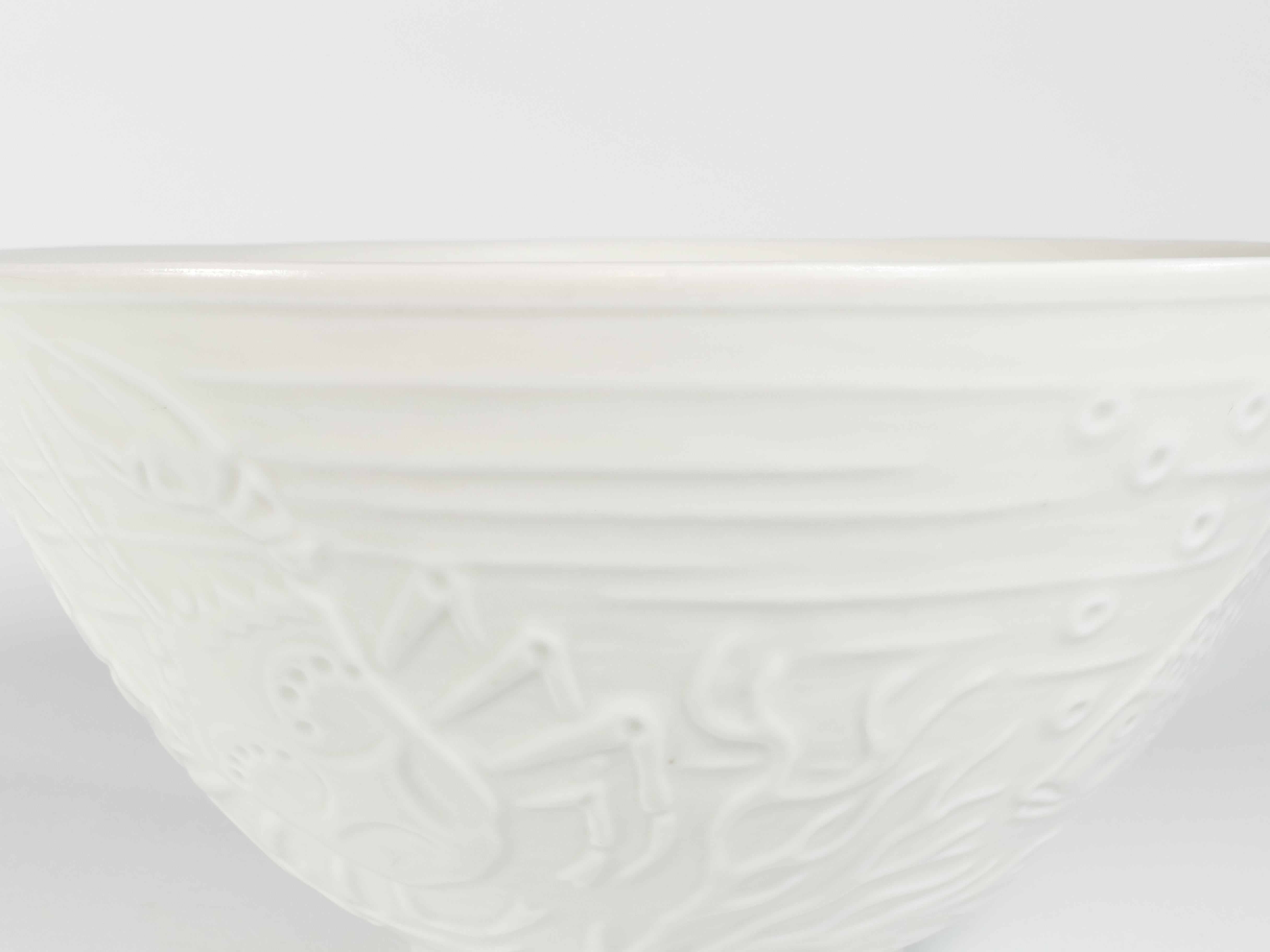  This is a large and thin, translucent white porcelain bowl designed by Gunnar Nylund for ALP Lidköping/Rörstrand. The bowl features a very handsome relief decoration depicting two fish, a crab, and an eel. The presence of the 
