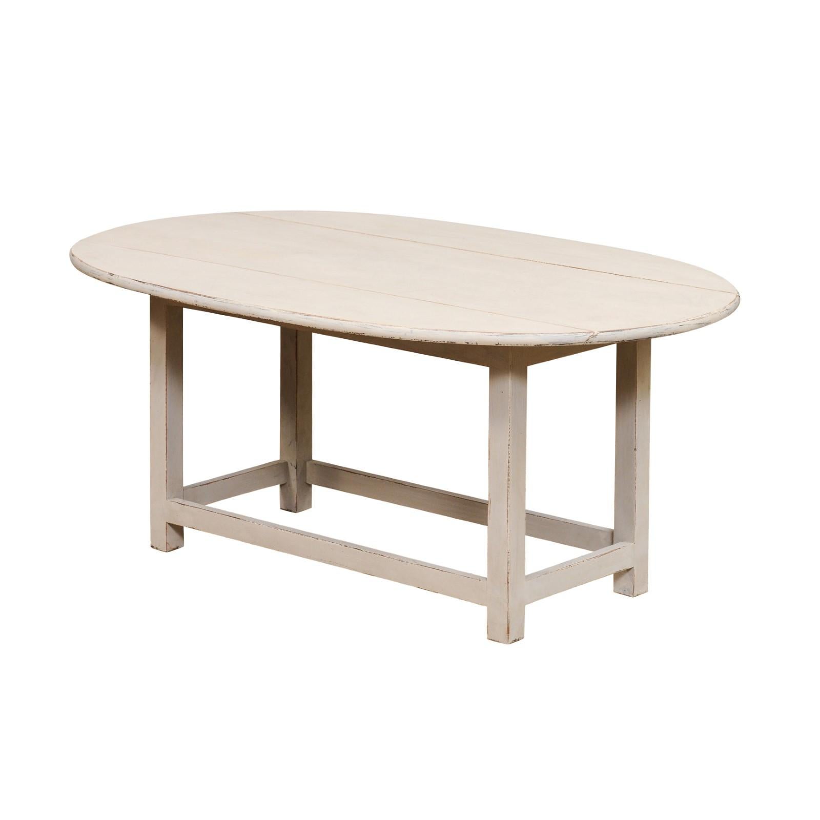 A Swedish oval painted coffee table with two drop leaves, straight legs and plain cross stretchers. Introducing a piece of Scandinavian charm, this Swedish oval painted coffee table with drop leaves, straight legs, and plain cross stretchers, dated