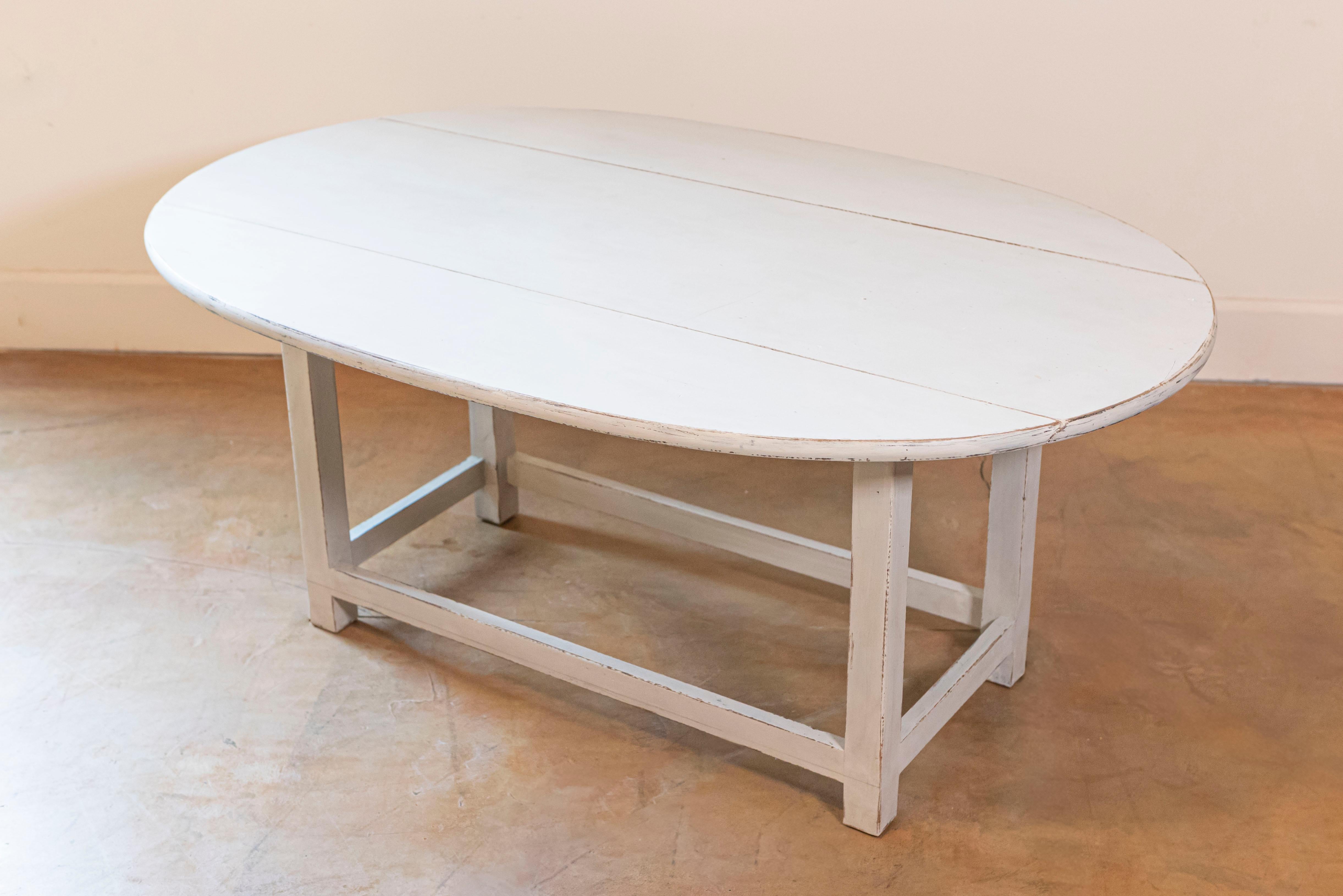 Table basse suédoise ovale peinte avec deux feuilles, pieds droits et traverses simples. Présentant un charme scandinave, cette table basse suédoise ovale peinte avec des feuilles tombantes, des pieds droits et des châssis croisés unis, datée du 20e