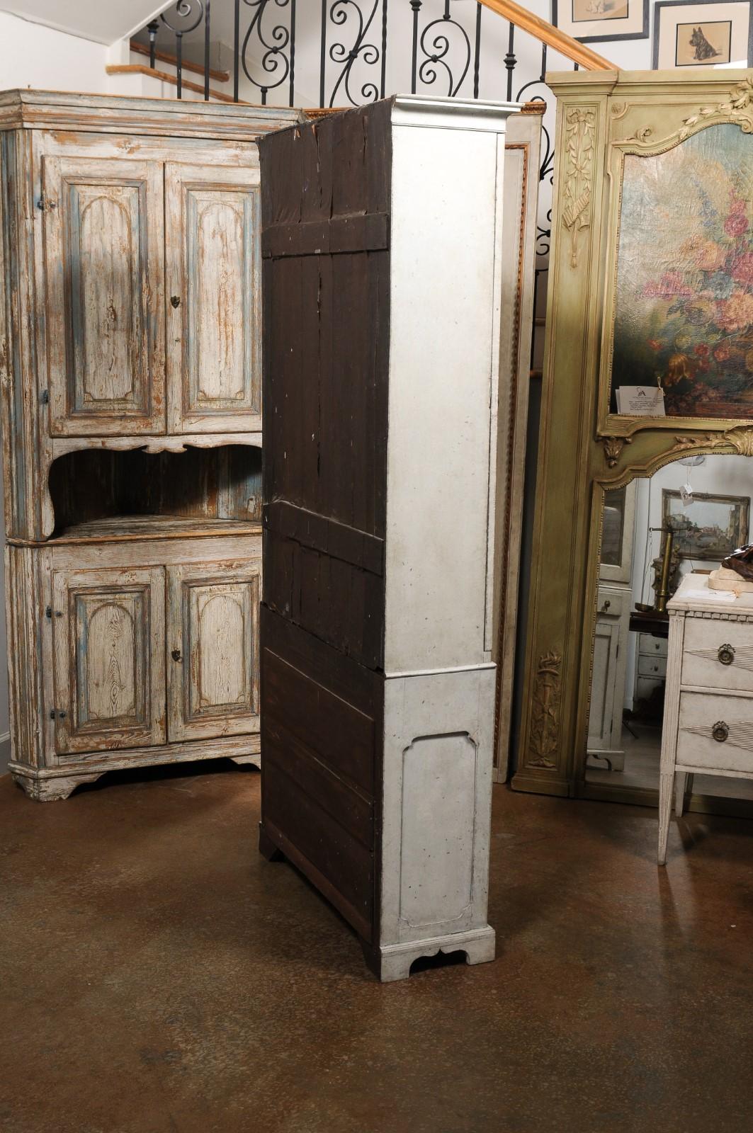 A Swedish Gustavian period painted wood two-part vitrine cabinet from the early 19th century, with single glass door, drawer and wooden doors. Created in Sweden during the first quarter of the 19th century, this painted cabinet features a cornice