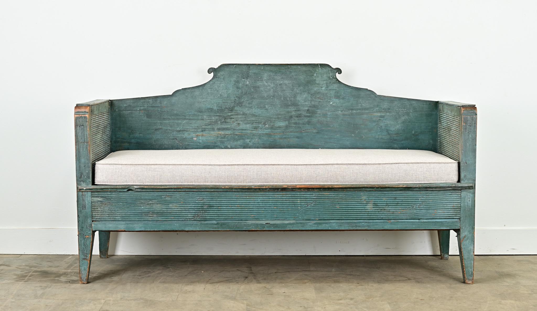 A Swedish Gustavian settle or bench from the 1790’s with its original paint finish. The frame of this Swedish bench is made of carved pine with its original worn blue paint finish. The flat back sits higher than the reeded bench arms and has a faint