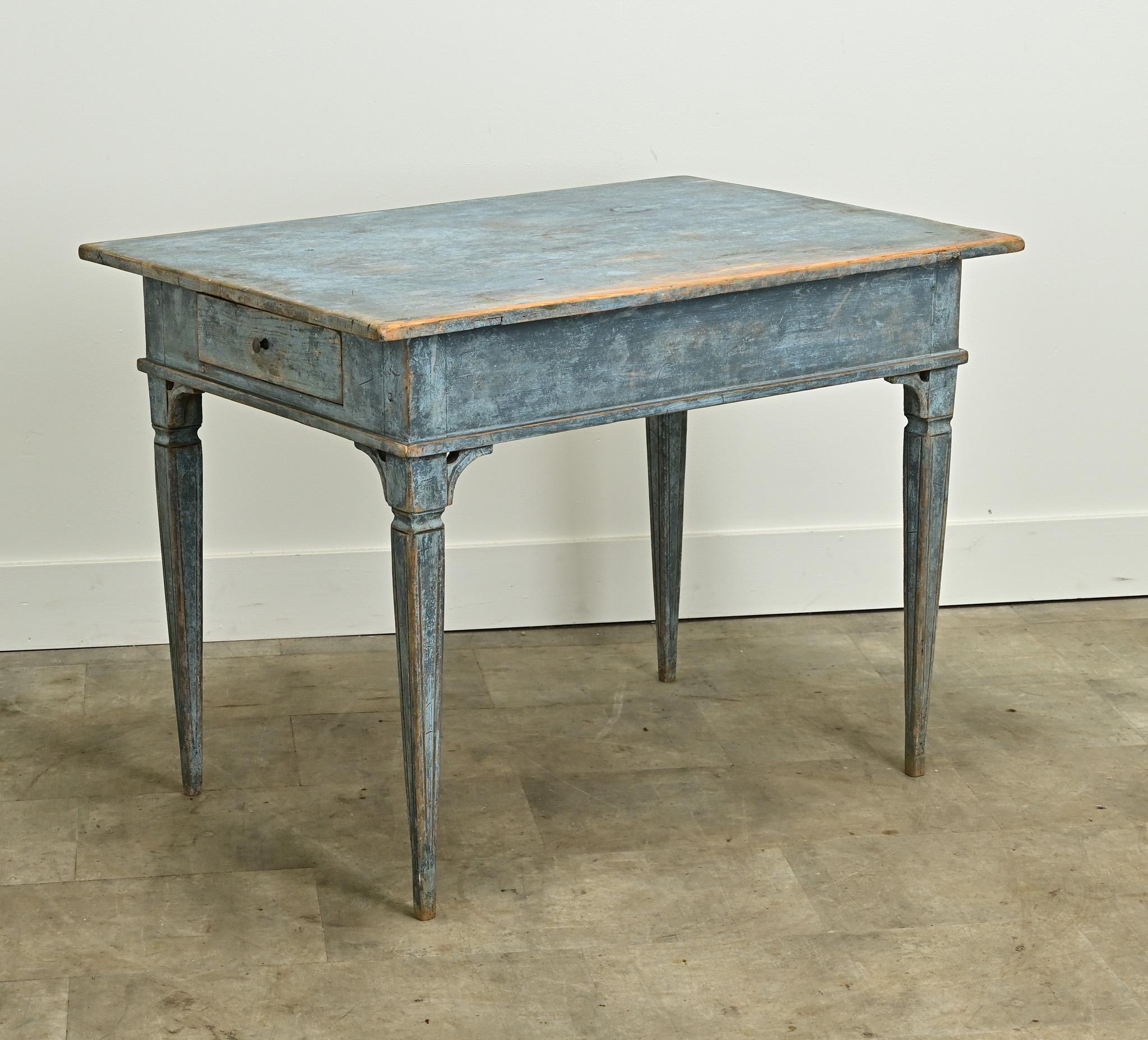 A Swedish Gustavian style center table is sure to make a statement in any interior. This table has its original worn blue painted finish and features a removable top over an apron with two drawers, each with a turned knob. The whole sits on tapered