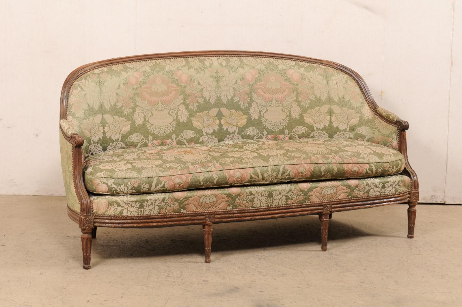 A Swedish period Gustavian upholstered and carved-wood sofa from the early 19th century. This antique tub style sofa from Sweden features an elegantly arched wooden top rail, with sides sloping down to become arms (fitted with manchette pad rests),
