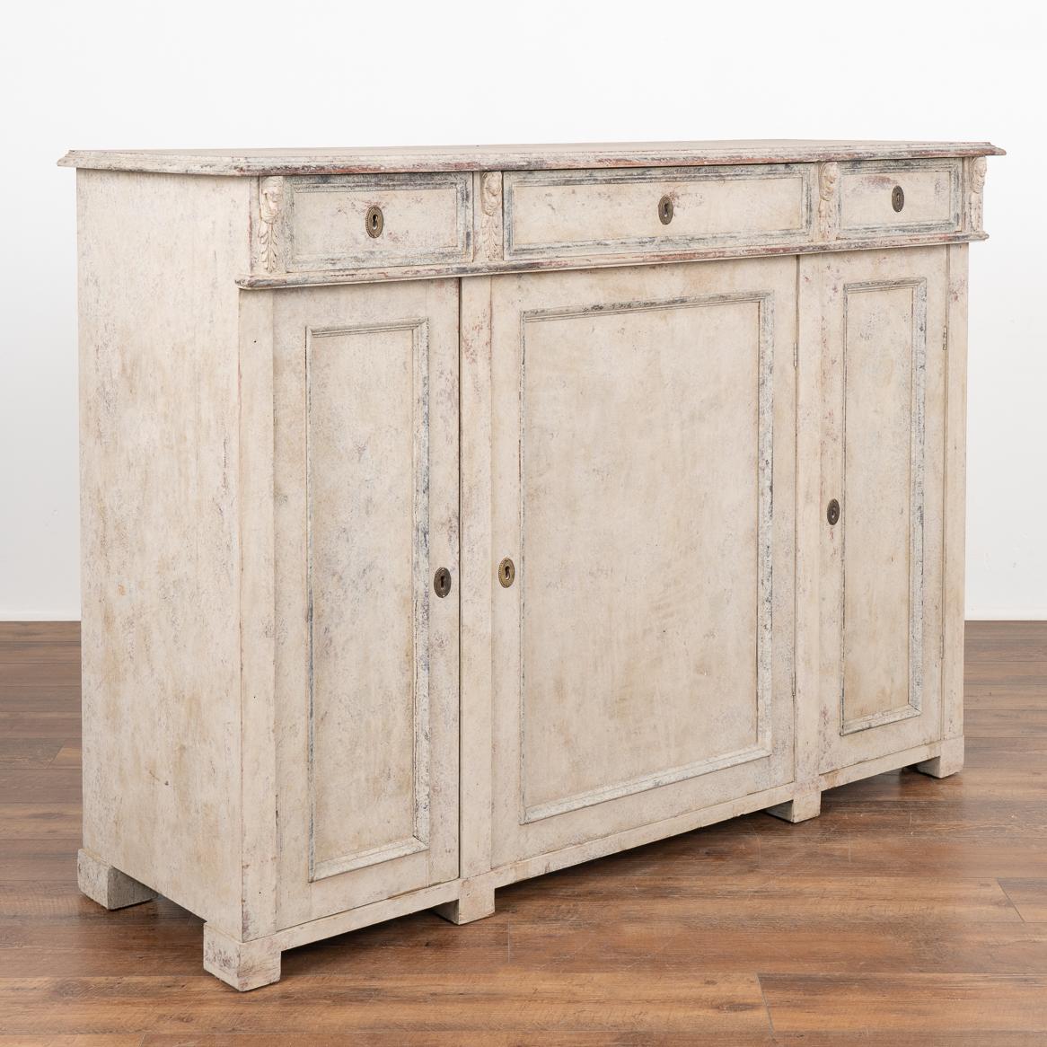 Gustavian gray painted tall pine sideboard with carved faces and acanthus leaves accenting the upper corners. 
Newer, professionally applied layered gray painted finish with plum undertones and muted blue/black accent around panel doors and drawers.