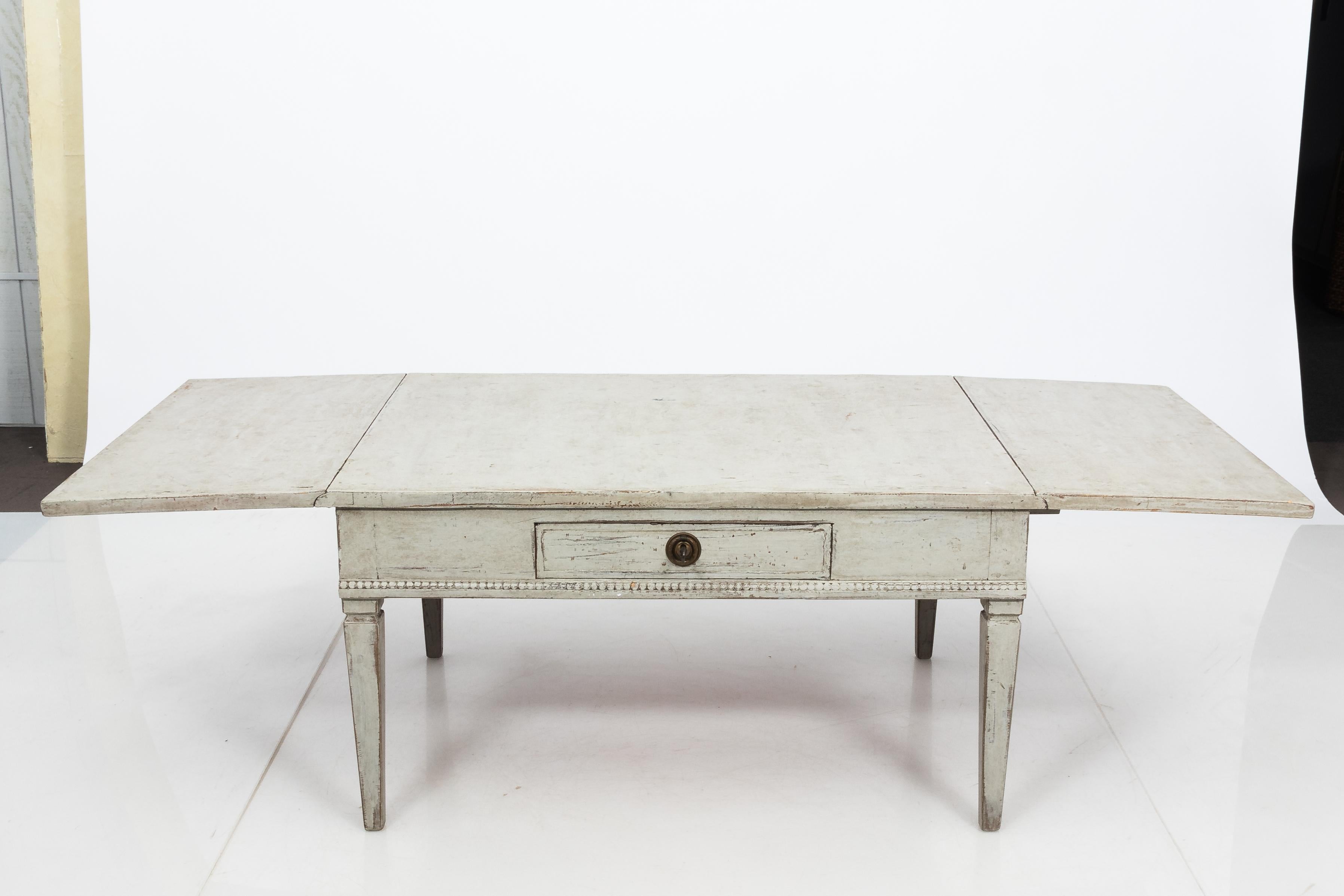 Unique Gustavian Style coffee table with drop leaves, made in Sweden circa 1850. The table is painted white with lovely patina from age. Decorated simply with beaded trim and sits on plain tapered legs. This versatile piece was likely a dining table