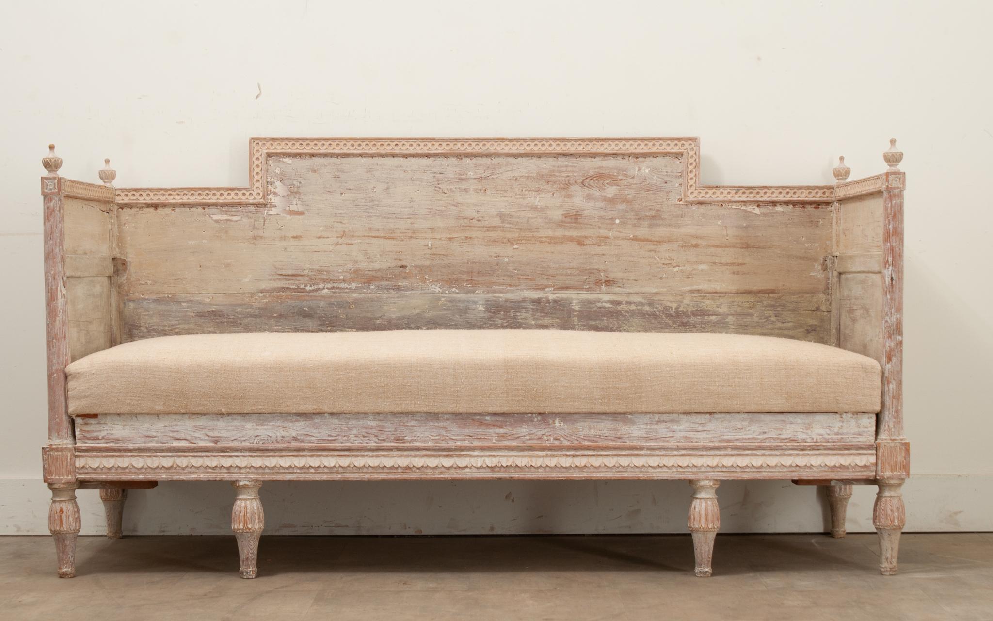 A Swedish 18th century Gustavian banquette with its original hand-scraped painted finish. The solidly constructed frame makes for a sheltering sofa as well, with a removable bench seat cushion. A hidden platform underneath slides out, cleverly