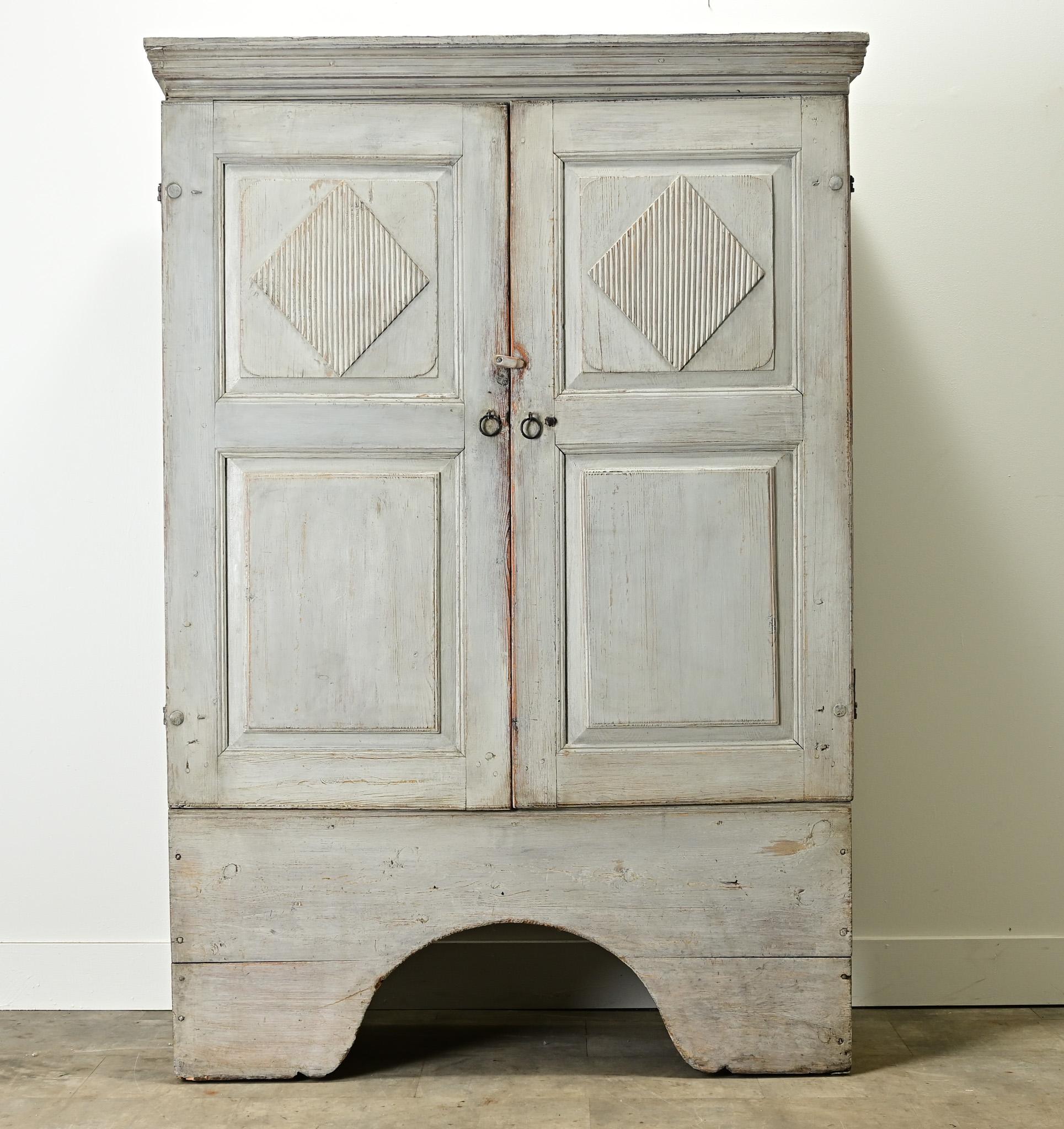 A painted Swedish Gustavian armoire from the late 1700’s. This solid pine cabinet has its original light gray-blue paint finish that is worn in all the right places. The tall paneled doors are carved with reeded diamond shape designs and open on