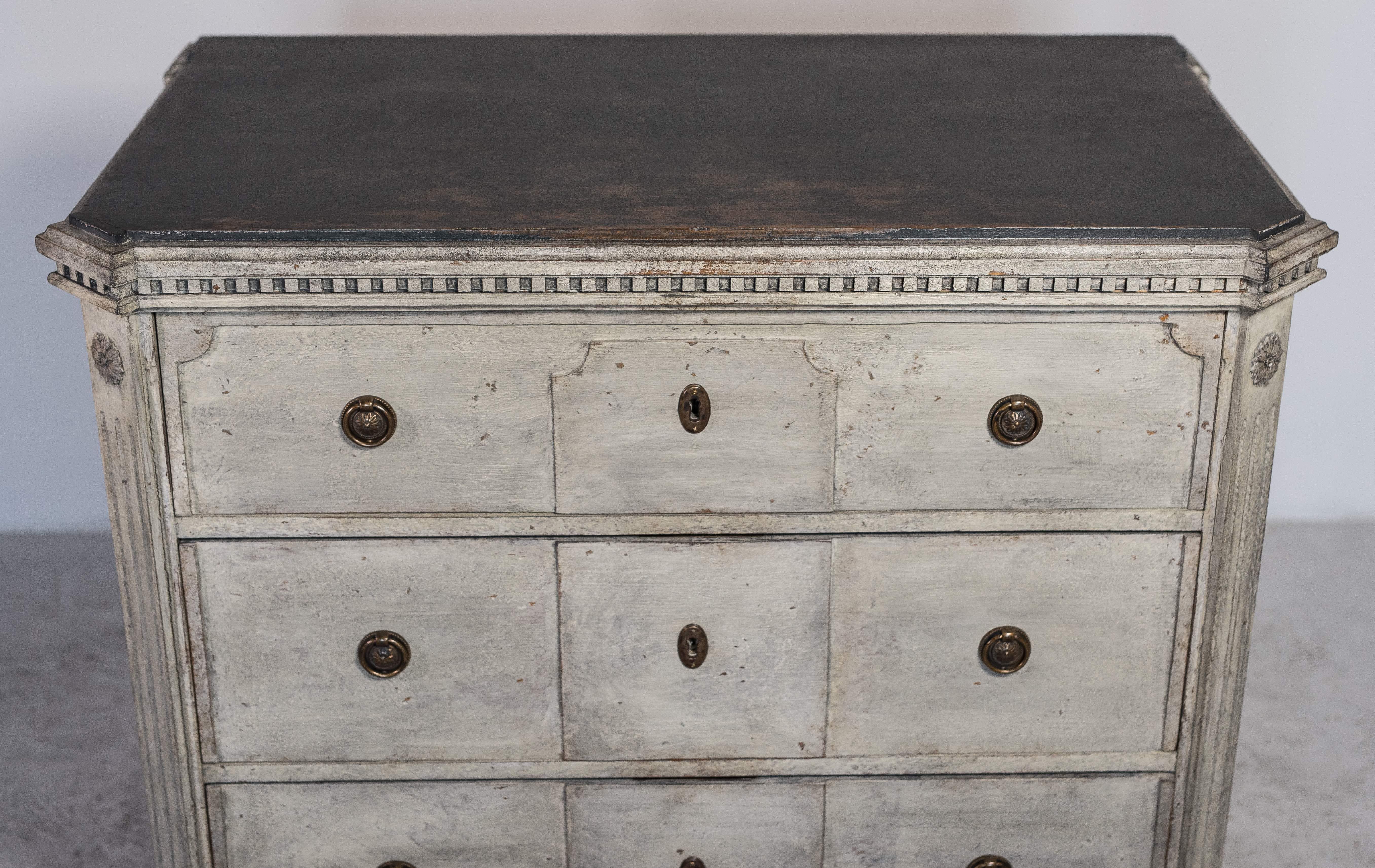 C 1870 antique Swedish Gustavian painted chest of drawers commode with detailed decorative motifs on the top rail and brass detailing.

It has 3 drawers with brass ring pulls and a carved plinth and feet with column detail on the front