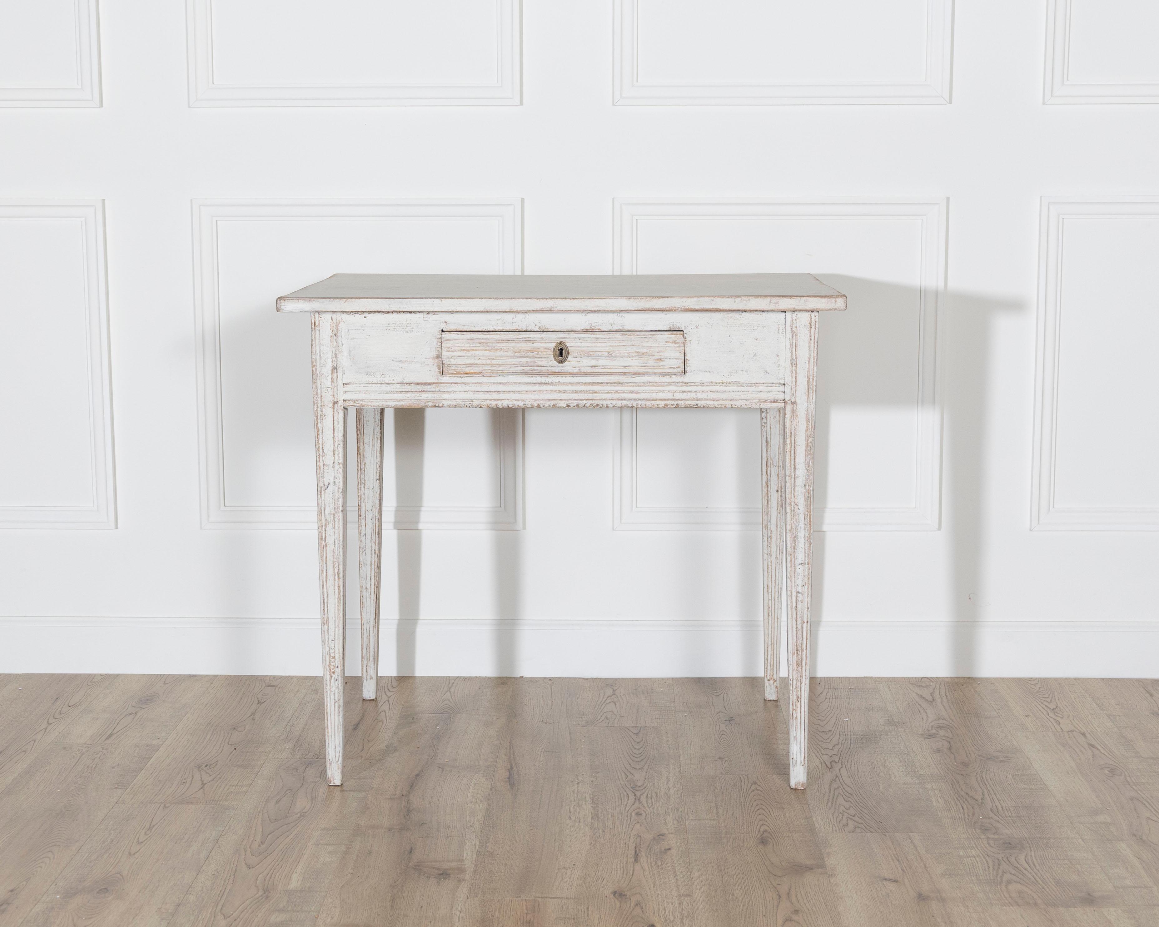 A Swedish Gustavian painted table from circa 1850, showcasing the refined simplicity of Scandinavian design. The rectangular top sits above a single drawer, adorned with linear fluting and a central escutcheon, offering both function and elegance.