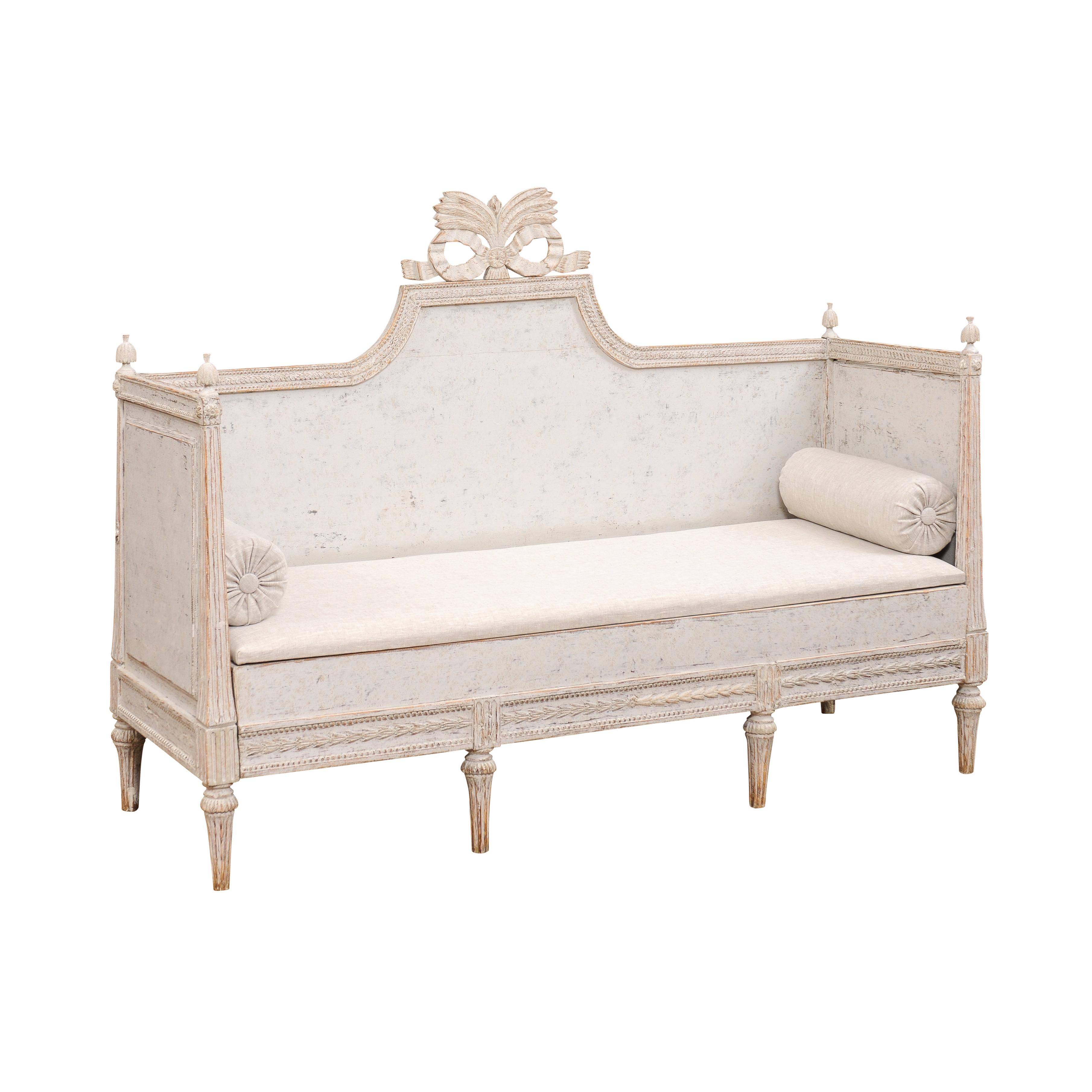 A Swedish Gustavian period painted wood sofa circa 1780 with carved crest, tall arms with finials, carved apron and cylindrical fluted legs. Step into the elegance of the Swedish Gustavian period with this exquisite painted wood sofa from the late