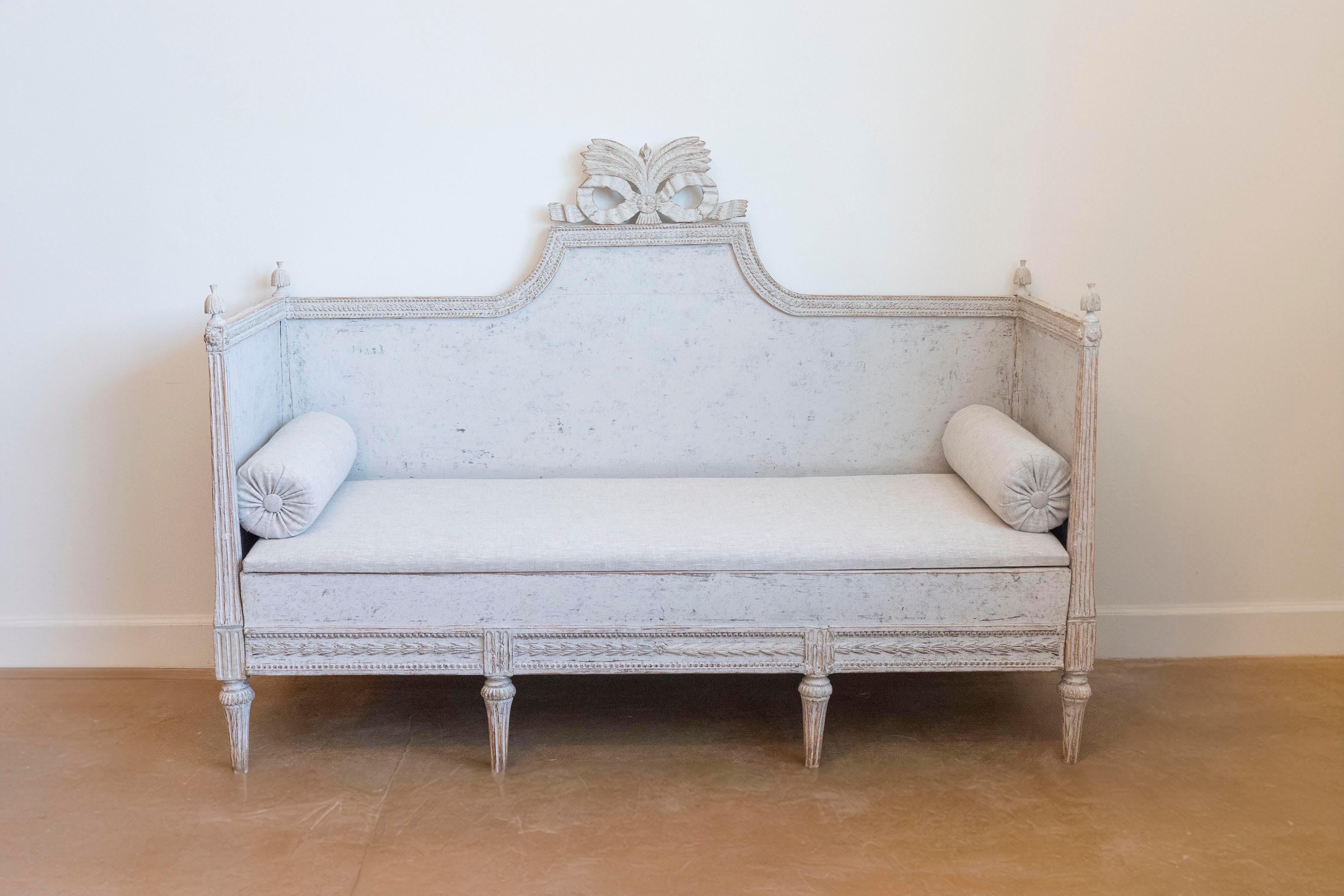A Swedish Gustavian period painted wood sofa circa 1780 with carved crest, tall arms with finials, carved apron and cylindrical fluted legs. Step into the elegance of the Swedish Gustavian period with this exquisite painted wood sofa from the late