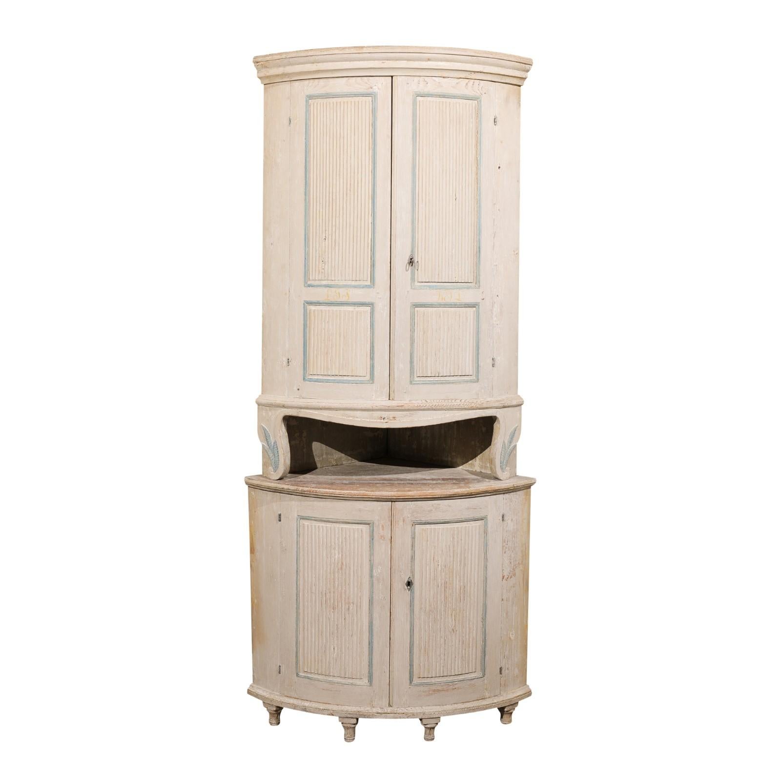 A Swedish Gustavian period painted wood two-part corner cabinet from the early 19th century, with reeded accents, foliage carving and open shelf. Created in Sweden during the Gustavian period in the early 19th century, this painted wood corner