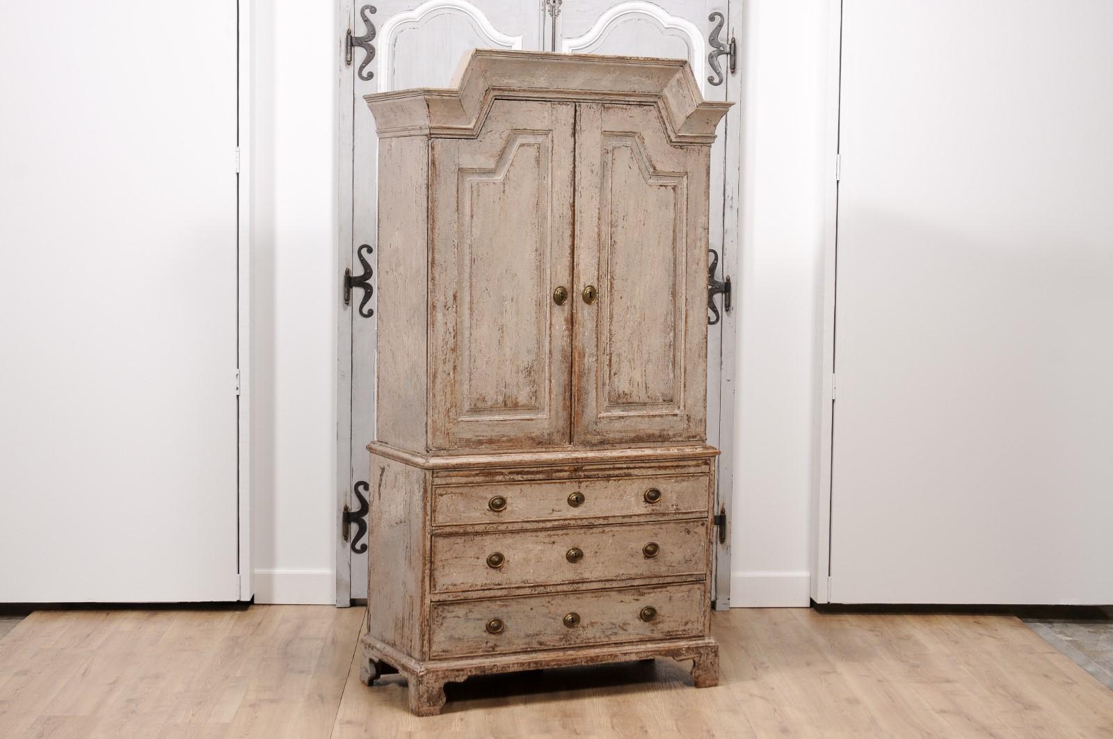 A Swedish Gustavian period painted wood cupboard from 1802 with broken pediment, two doors, three drawers, bracket feet and distressed patina. Experience the epitome of Swedish Gustavian design with this breathtaking painted wood cupboard from 1802,