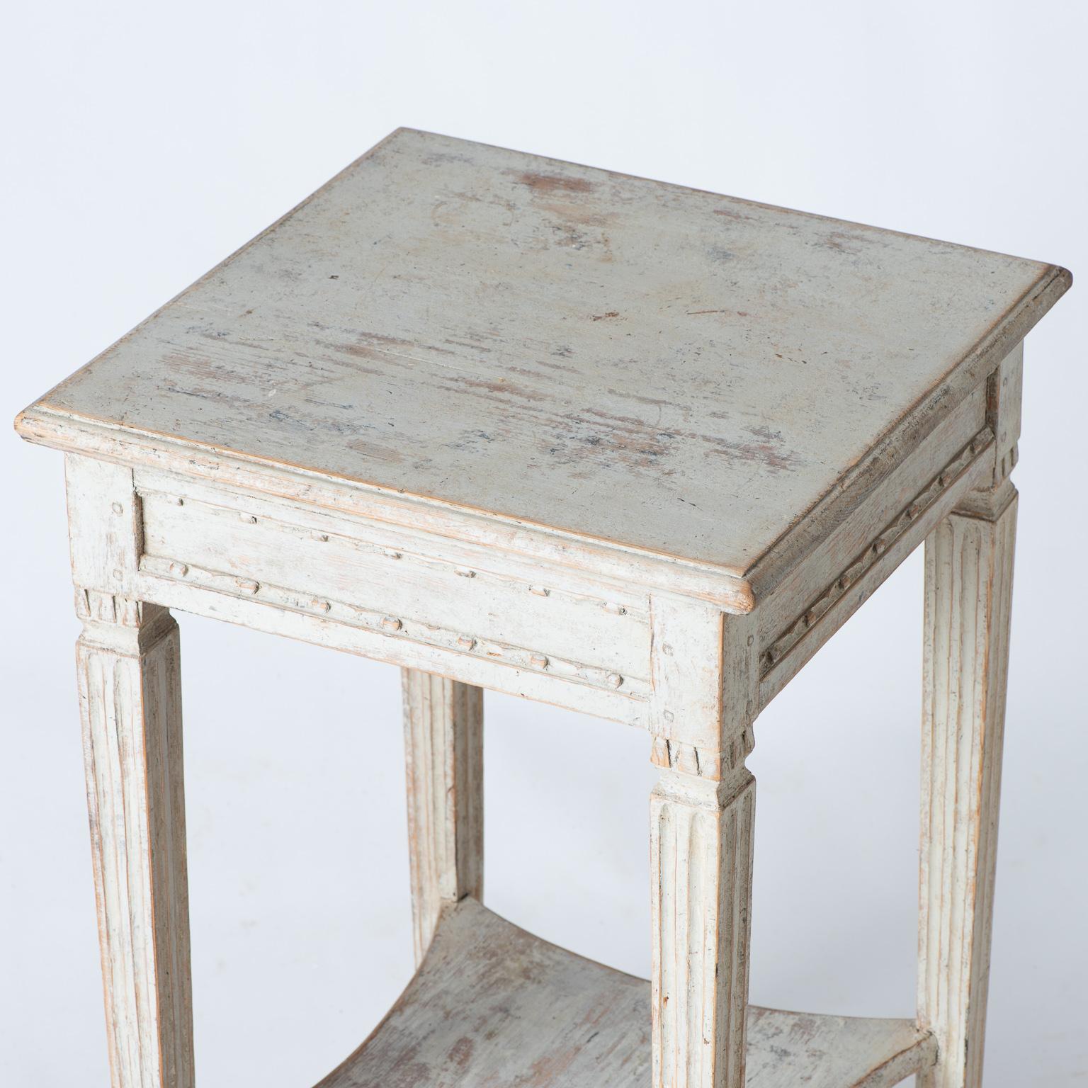 This elegant table from the Gustavian period has refined details, including carvings around the apron, and distinctly reeded legs framing the indented bottom shelf. The pale cream paint surface is original. The table is an ideal size to fit in many