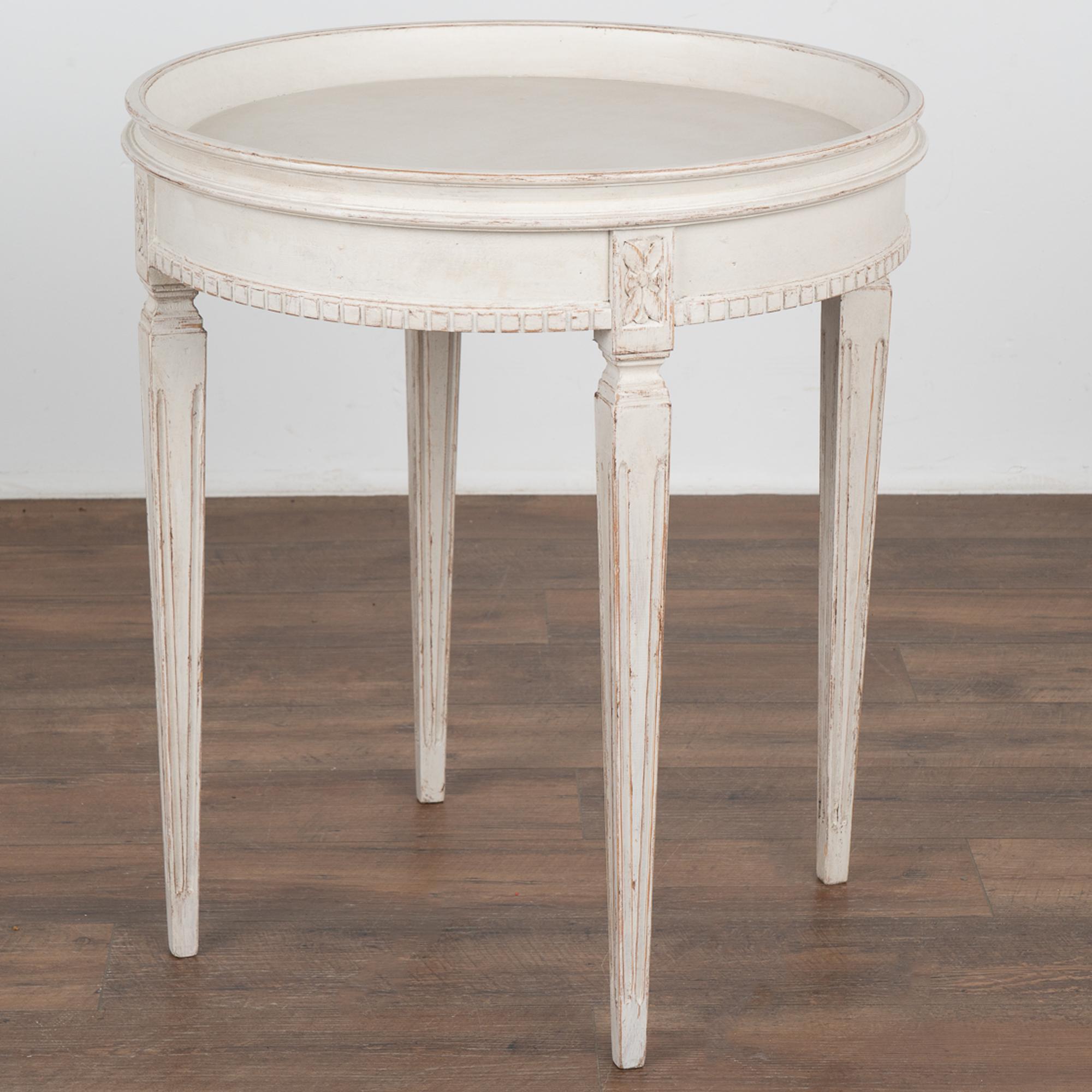 Lovely round Swedish Gustavian side table with carved dentil molding and tapered fluted legs topped by carved floral accents.
Newer, professionally applied layered white painted finish which is lightly distressed, adds to the charm of this graceful