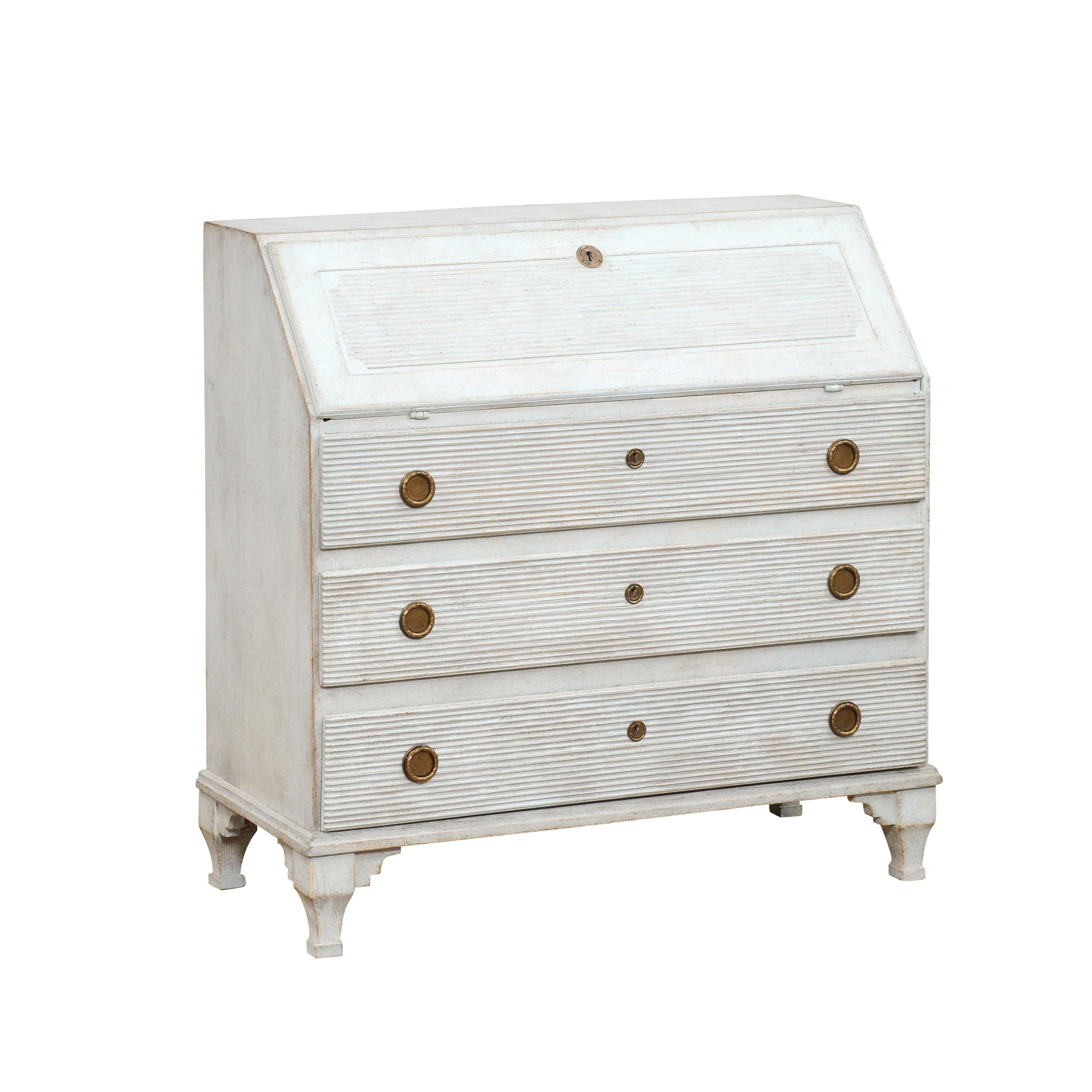 A Swedish Gustavian style painted wood secretary circa 1820 with slant front desk, carved fluted motifs, three drawers and carved feet. Transport yourself to the elegant Swedish Gustavian style with this charming painted wood secretary from the
