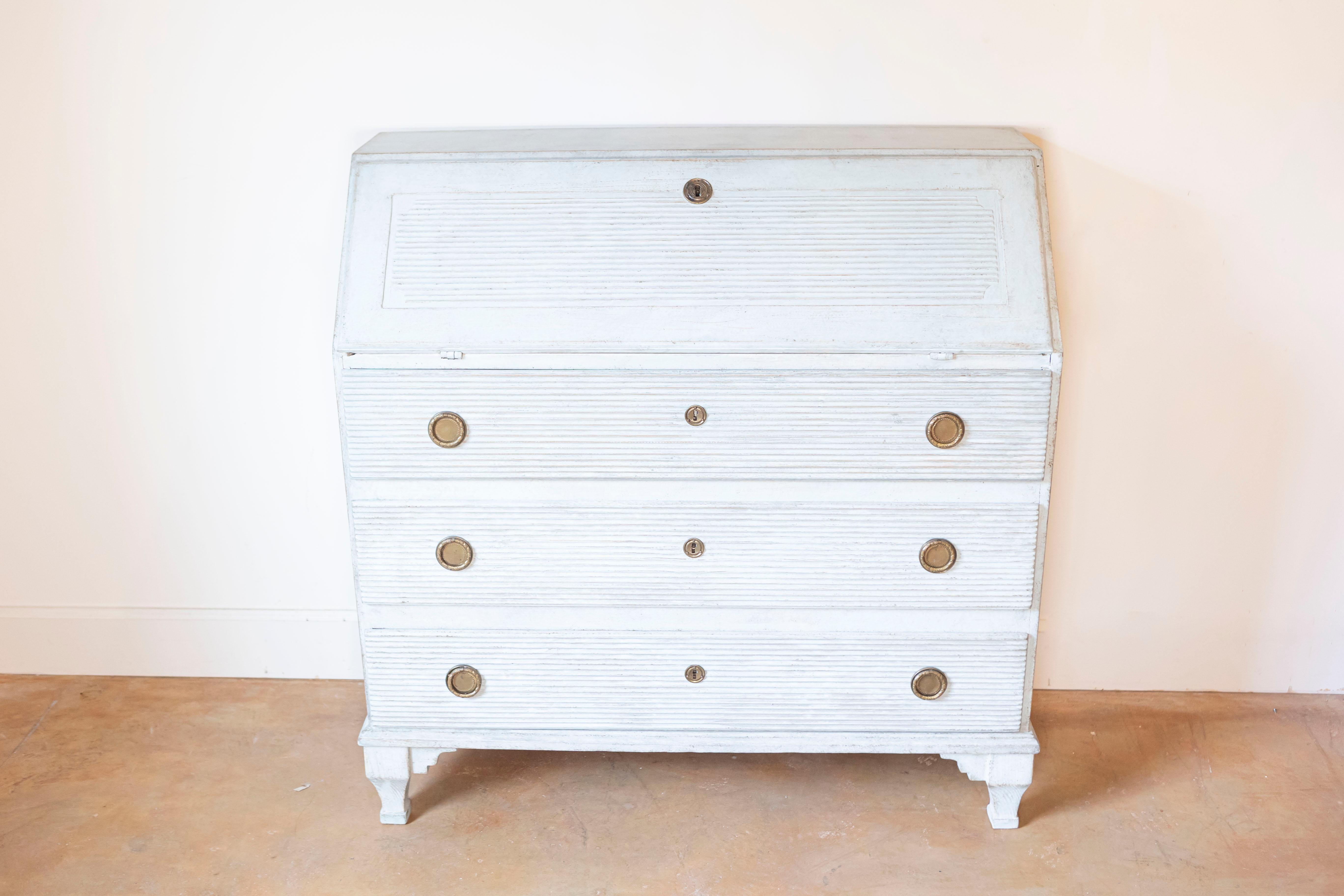 A Swedish Gustavian style painted wood secretary circa 1820 with slant front desk, carved fluted motifs, three drawers and carved feet. Transport yourself to the elegant Swedish Gustavian style with this charming painted wood secretary from the