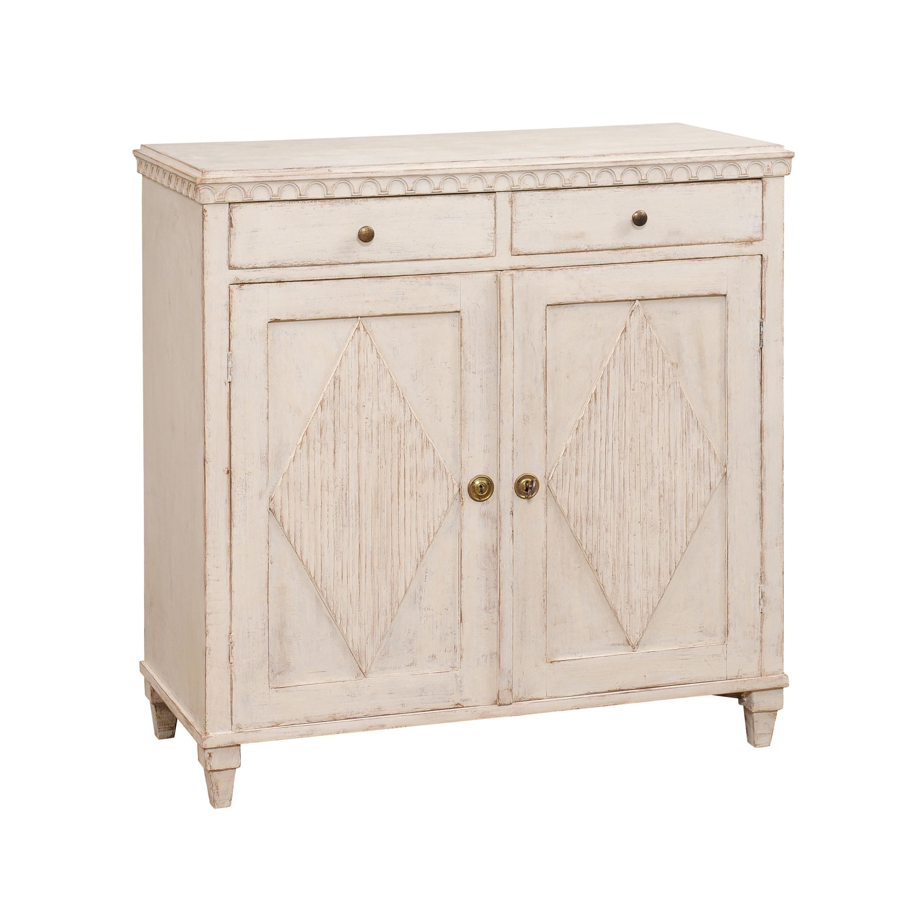 A Swedish Gustavian style painted wood sideboard from circa 1840 with two drawers over two doors and carved diamond motifs. Infuse your space with a touch of Swedish elegance and practicality with this Gustavian-style painted wood sideboard from