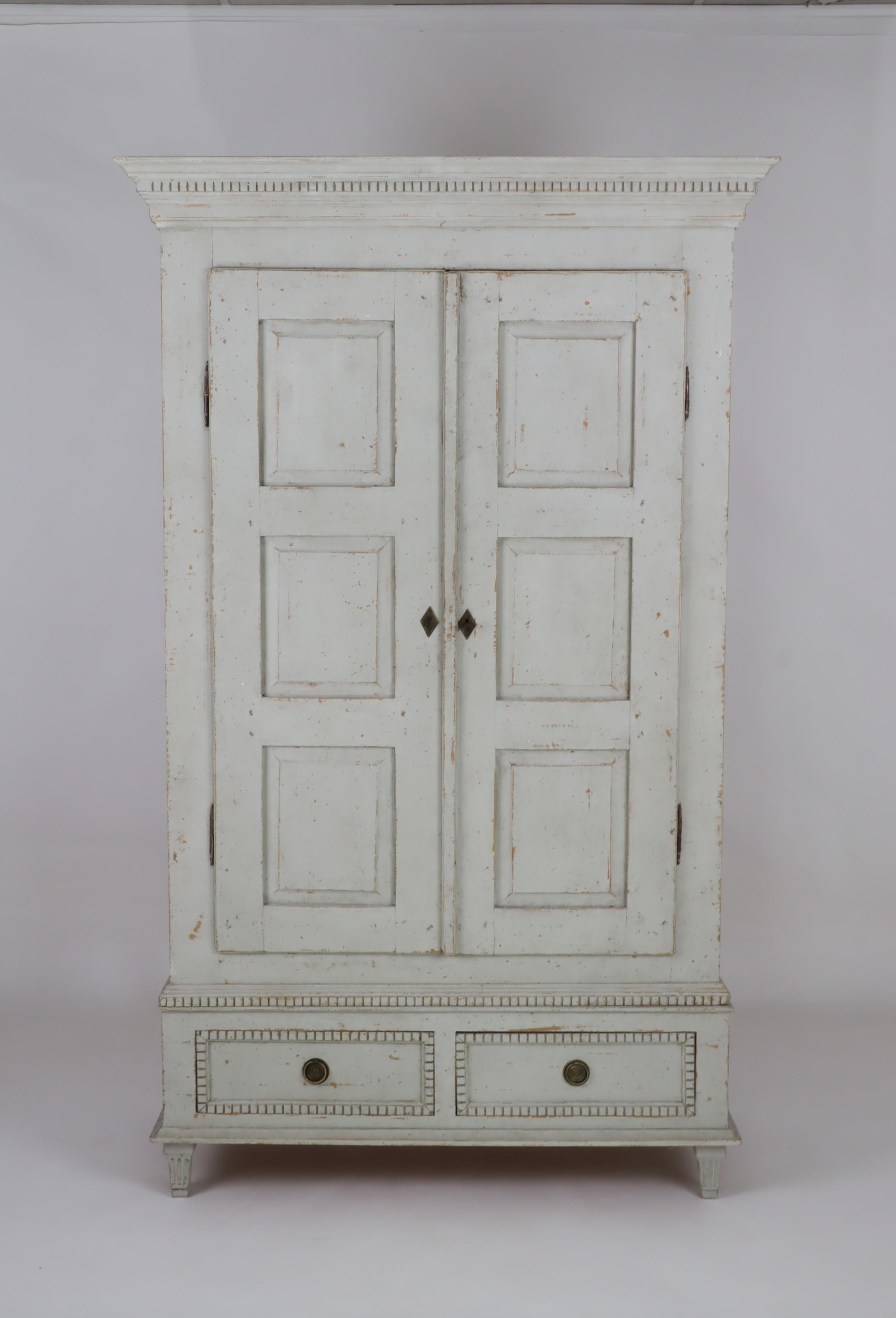 A Swedish Gustavian style painted wood wardrobe from circa 1850 with two doors and two lower drawers. This Swedish Gustavian style painted wardrobe, crafted circa 1850, manifests the grace of historical craftsmanship. The serene hue of the light