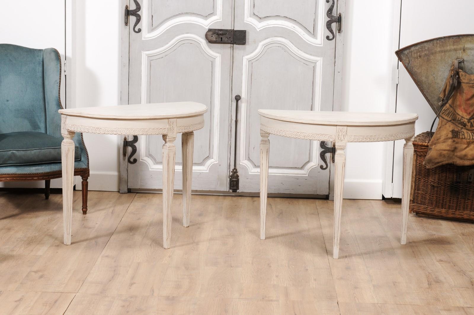 A pair of Swedish Gustavian style painted wood demi-lune console tables from circa 1850 with carved guilloche motifs, tapered legs with fluted accents and carved rosettes on the knees. Indulge in the exquisite design of this pair of Swedish