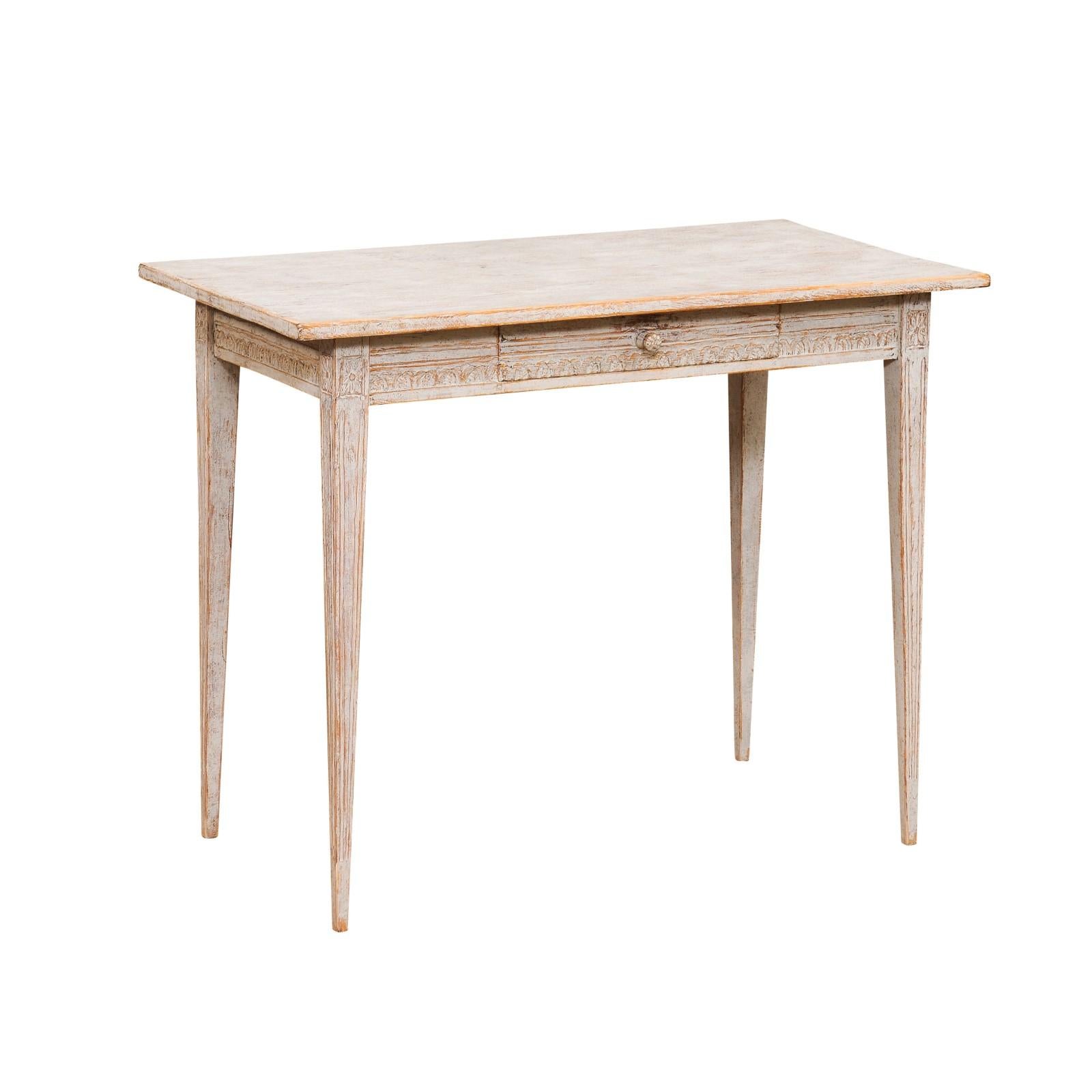 A Swedish Gustavian style wooden desk circa 1850 with carved apron, single drawer, tapered legs and distressed finish. Immerse yourself in the charm of 19th-century Scandinavia with this Swedish Gustavian style wooden desk, circa 1850. Boasting a