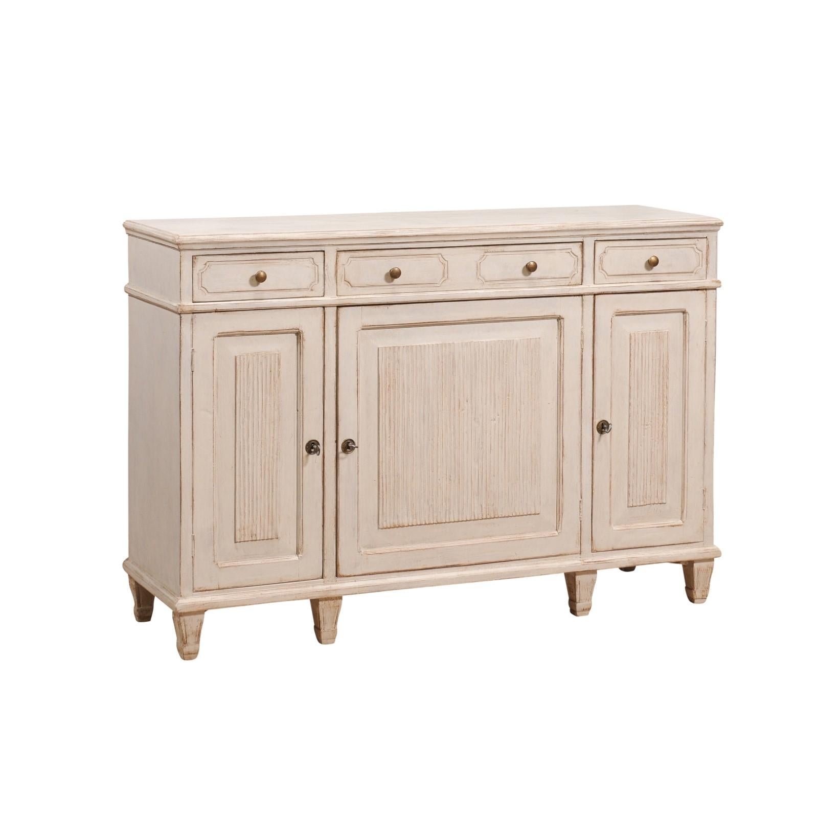 A Swedish Gustavian style sideboard from circa 1870 with three drawers over three doors, carved reeded motifs and light gray painted finish. This Swedish Gustavian style sideboard, dating back to circa 1870, is a splendid example of classic