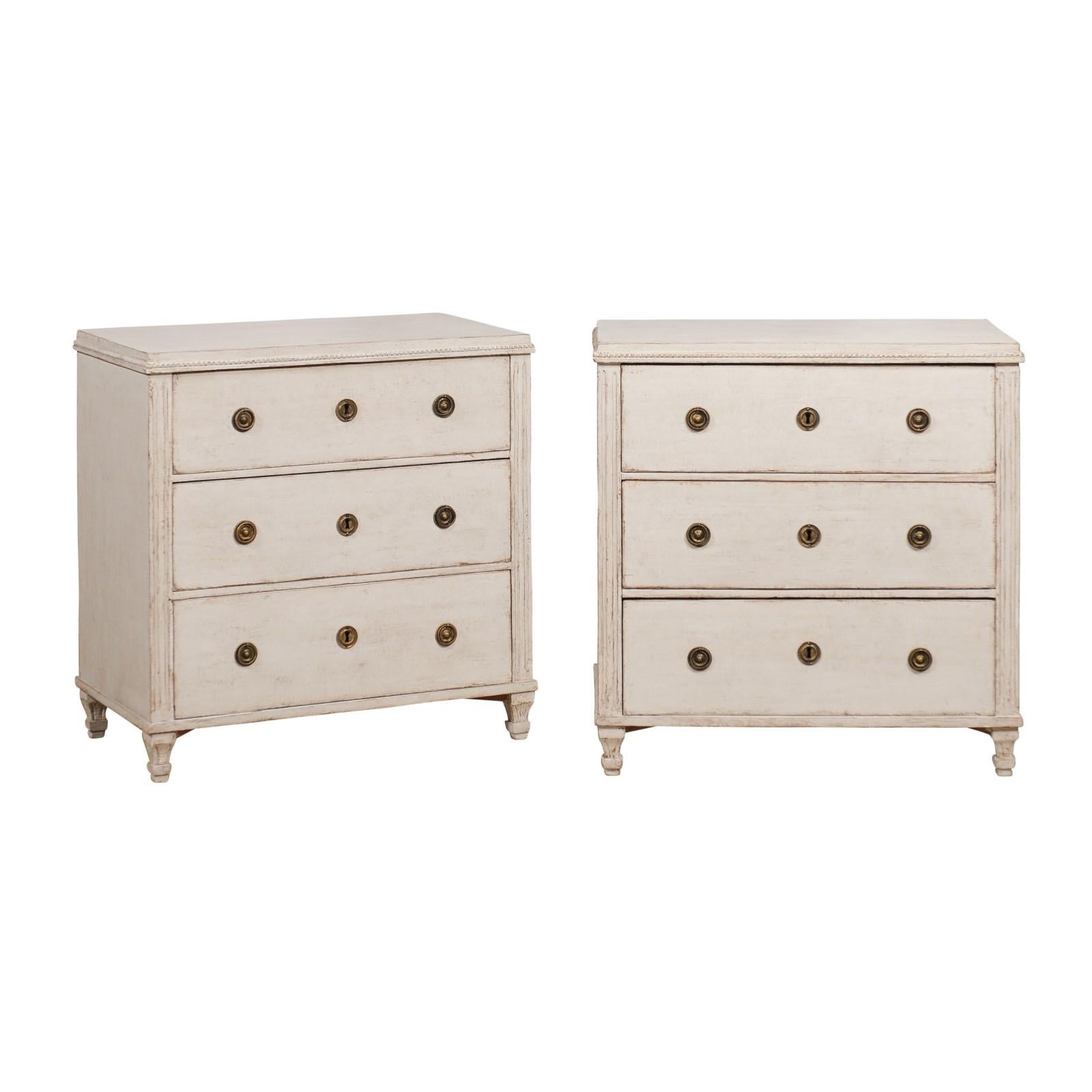 A pair of Swedish Gustavian style three-drawer chests from circa 1880 with gray/beige painted finish, petite carved beads and flutes side posts. Imbued with the tranquil charm characteristic of Swedish Gustavian style, this pair of three-drawer