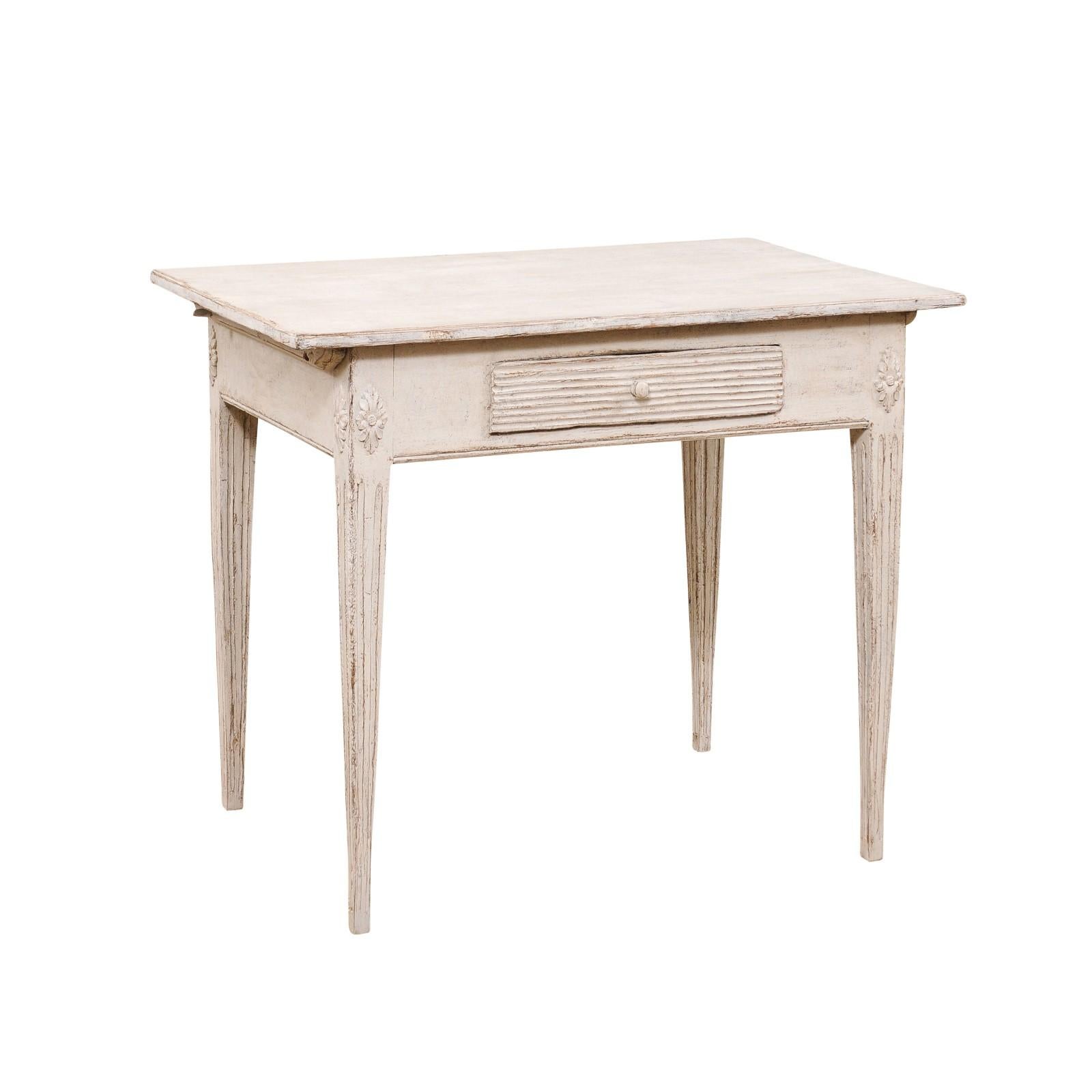 A Swedish Gustavian style painted wood side table from the late 19th century, with reeded drawer, carved rosettes and fluted legs. Created in Sweden during the last quarter of the 19th century, this painted side table features a rectangular top