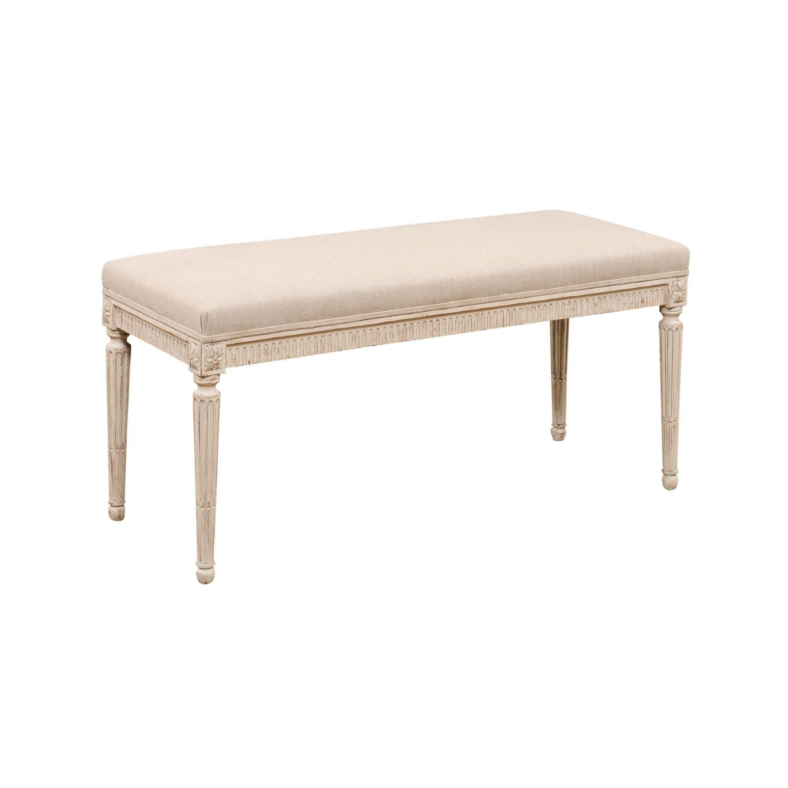 A Swedish Gustavian style painted wood bench from the late 19th century with lift-top, fluted apron, carved rosettes and cylindrical tapering legs. Created in Sweden during the last quarter of the 19th century, this painted bench features a