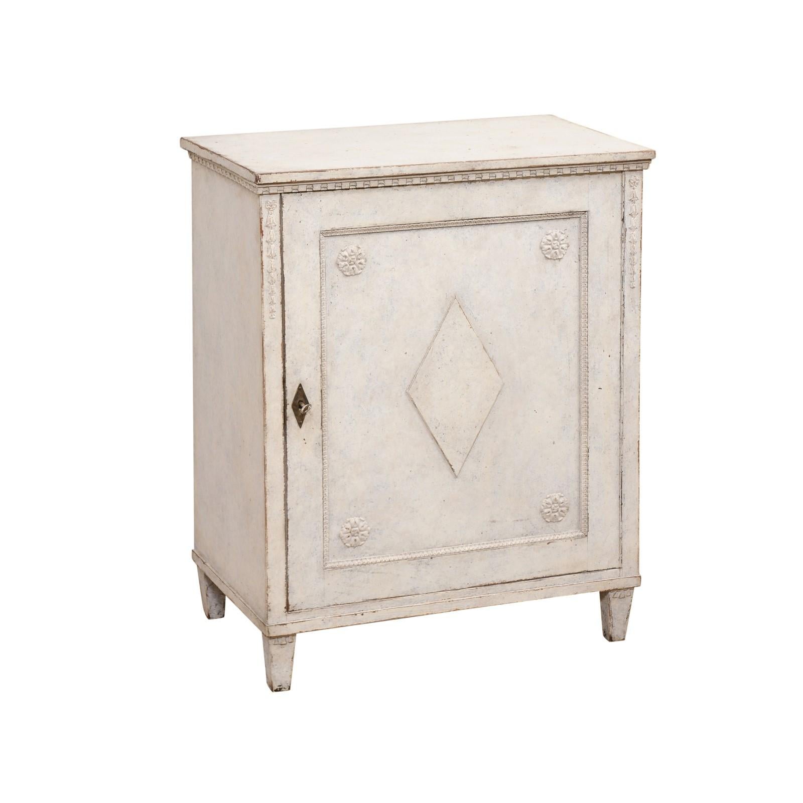 A Swedish Gustavian style painted wood cabinet from the late 19th century, with single door, carved rosettes, diamond motifs and dentil molding. Created in Sweden during the last quarter of the 19th century, this painted cabinet features a