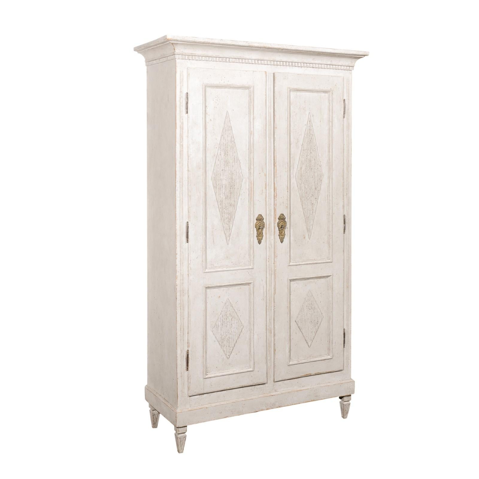 A Swedish Gustavian style painted wood linen cabinet from the late 19th century, with carved dentil molding and reeded diamond motifs. Created in Sweden during the last quarter of the 19th century, this painted wood cabinet features a curving