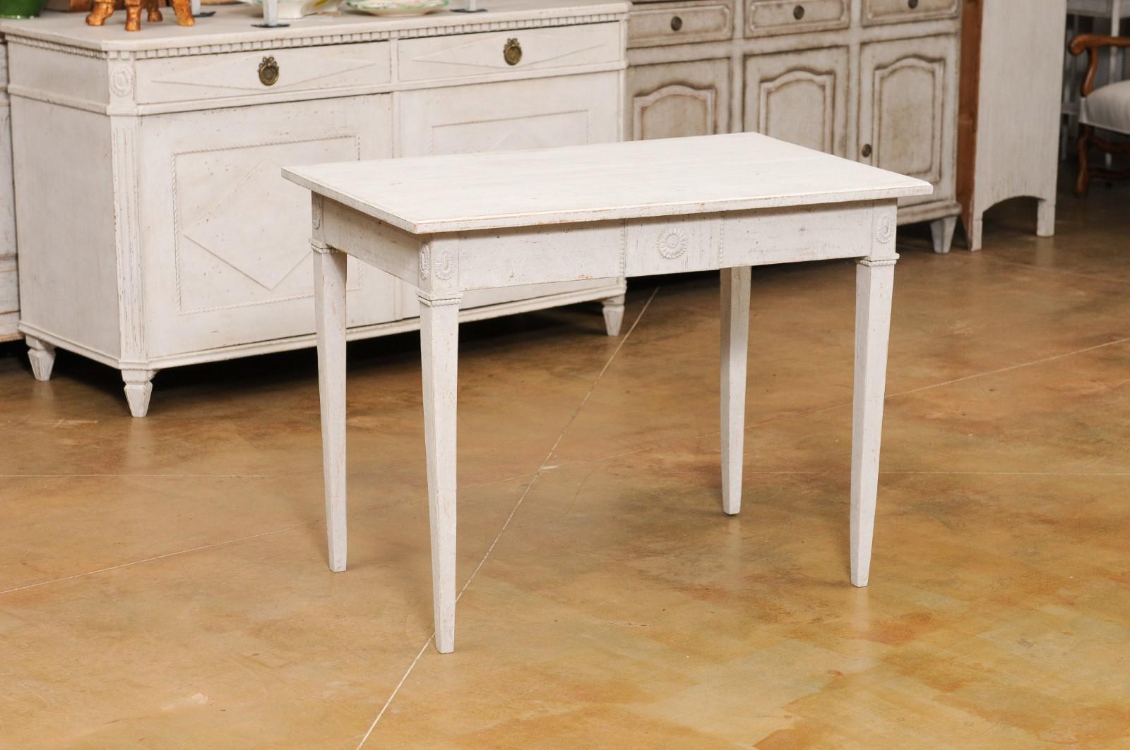 A Swedish Gustavian style painted wood table from the late 19th century, with carved rosettes and tapered legs. Created in Sweden during the last quarter of the 19th century, this painted table features a rectangular top sitting above an apron