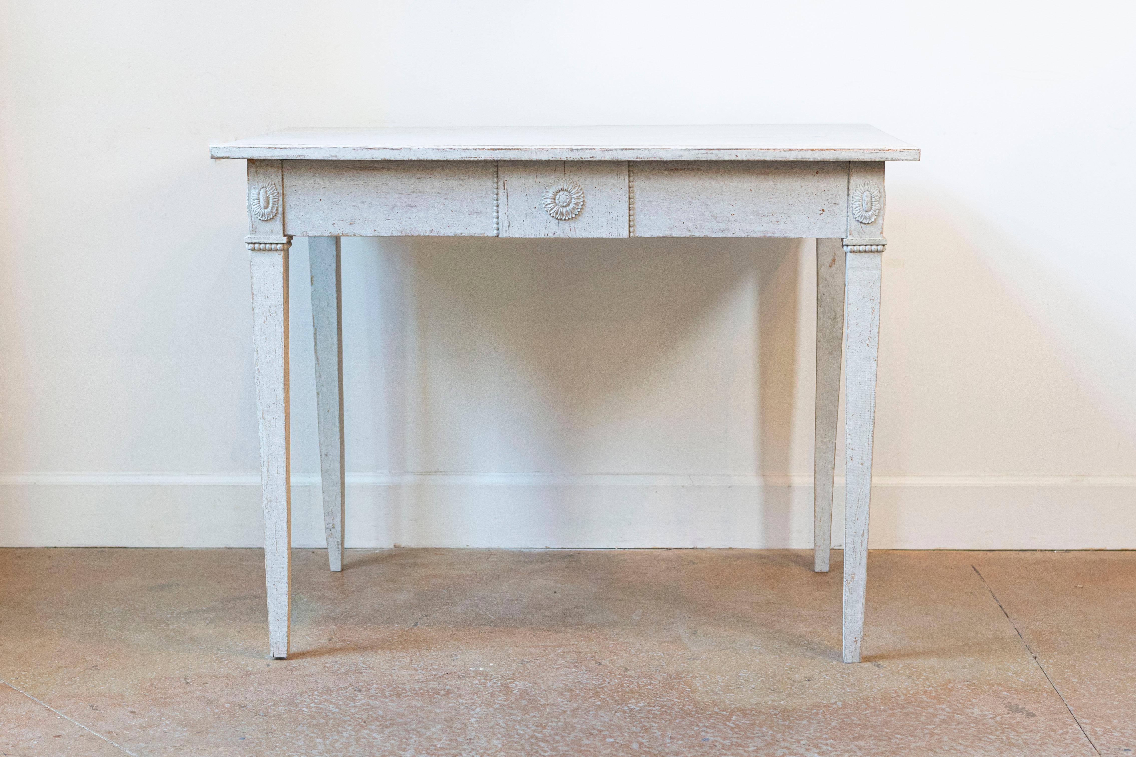 A Swedish Gustavian style painted wood table from the late 19th century, with carved rosettes and tapered legs. Created in Sweden during the last quarter of the 19th century, this painted table features a rectangular top sitting above an apron