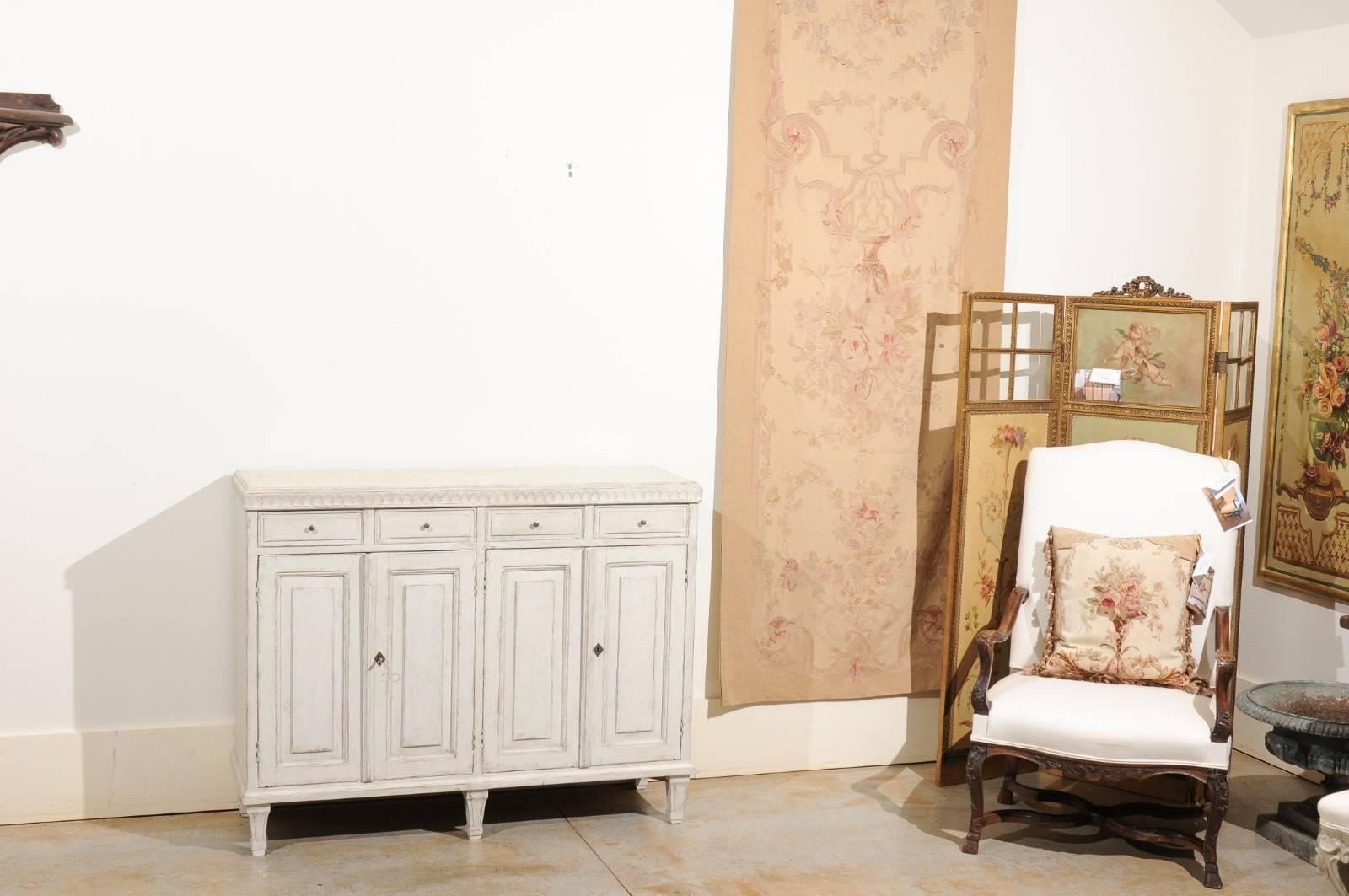 A Swedish Gustavian style late 19th century painted wood buffet from Stockholm with carved molding, four doors, four drawers and tapered feet. This exquisite Swedish buffet features a slightly raised, rectangular top, sitting above a carved molding