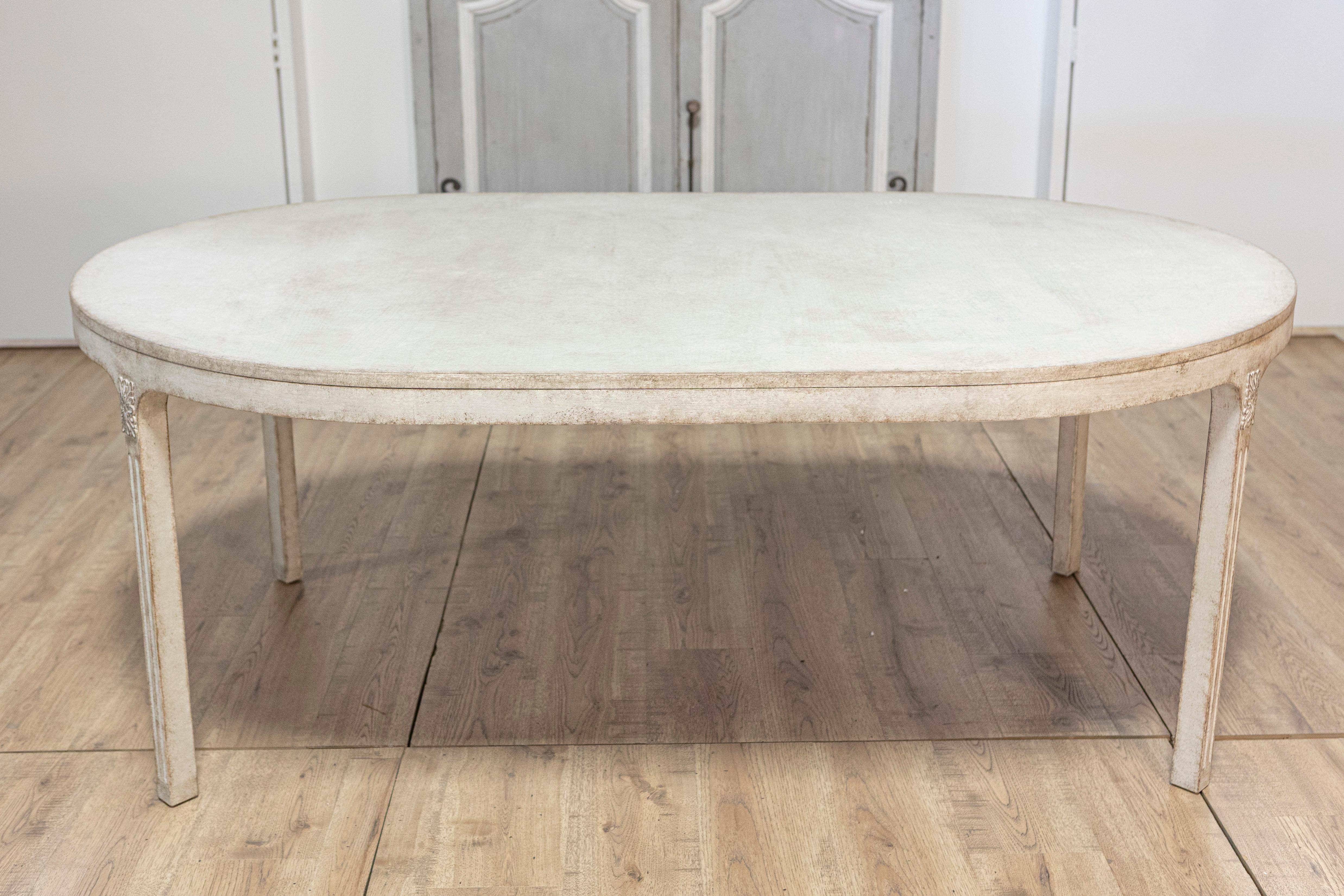 A Swedish oval top dining table from circa 1890 with light Gustavian gray painted finish and carved elongated rosettes on the knees. Created in Sweden around 1890, this exquisite dining table captures the essence of Gustavian elegance with its light