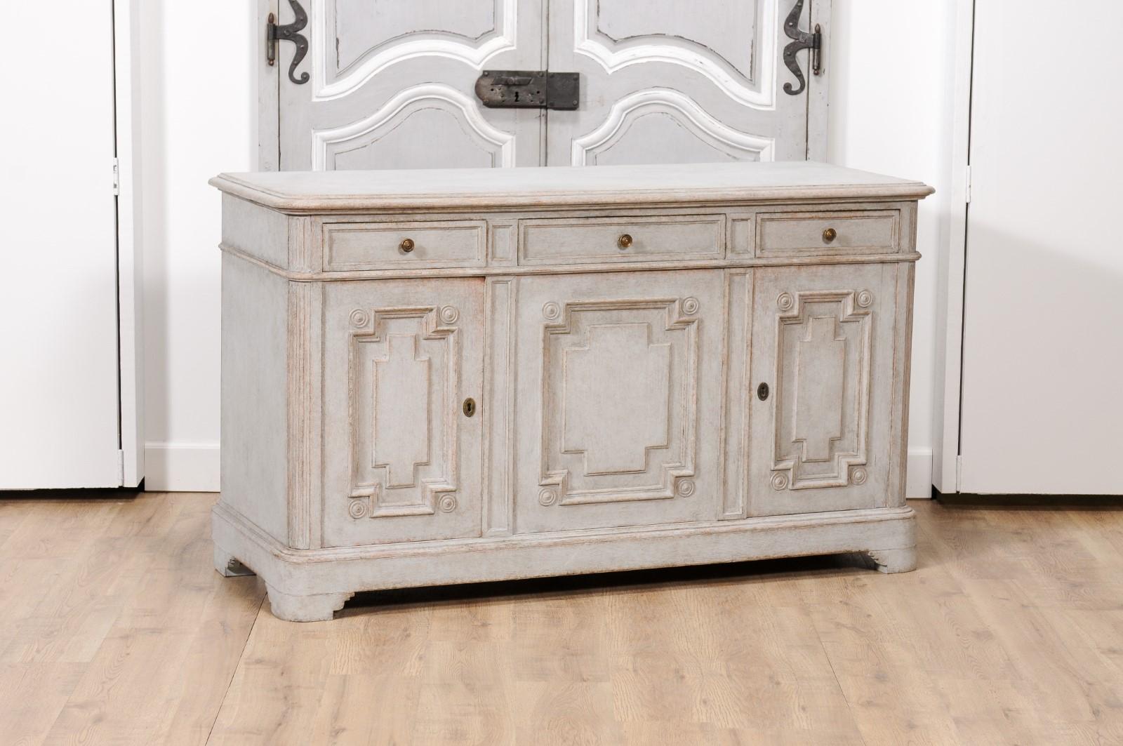 A Swedish Gustavian style painted wood sideboard from circa 1890 with three drawers over three doors, fluted side posts, carved bracket feet and carved geometric motifs. Imbued with the timeless elegance of Swedish Gustavian design, this painted
