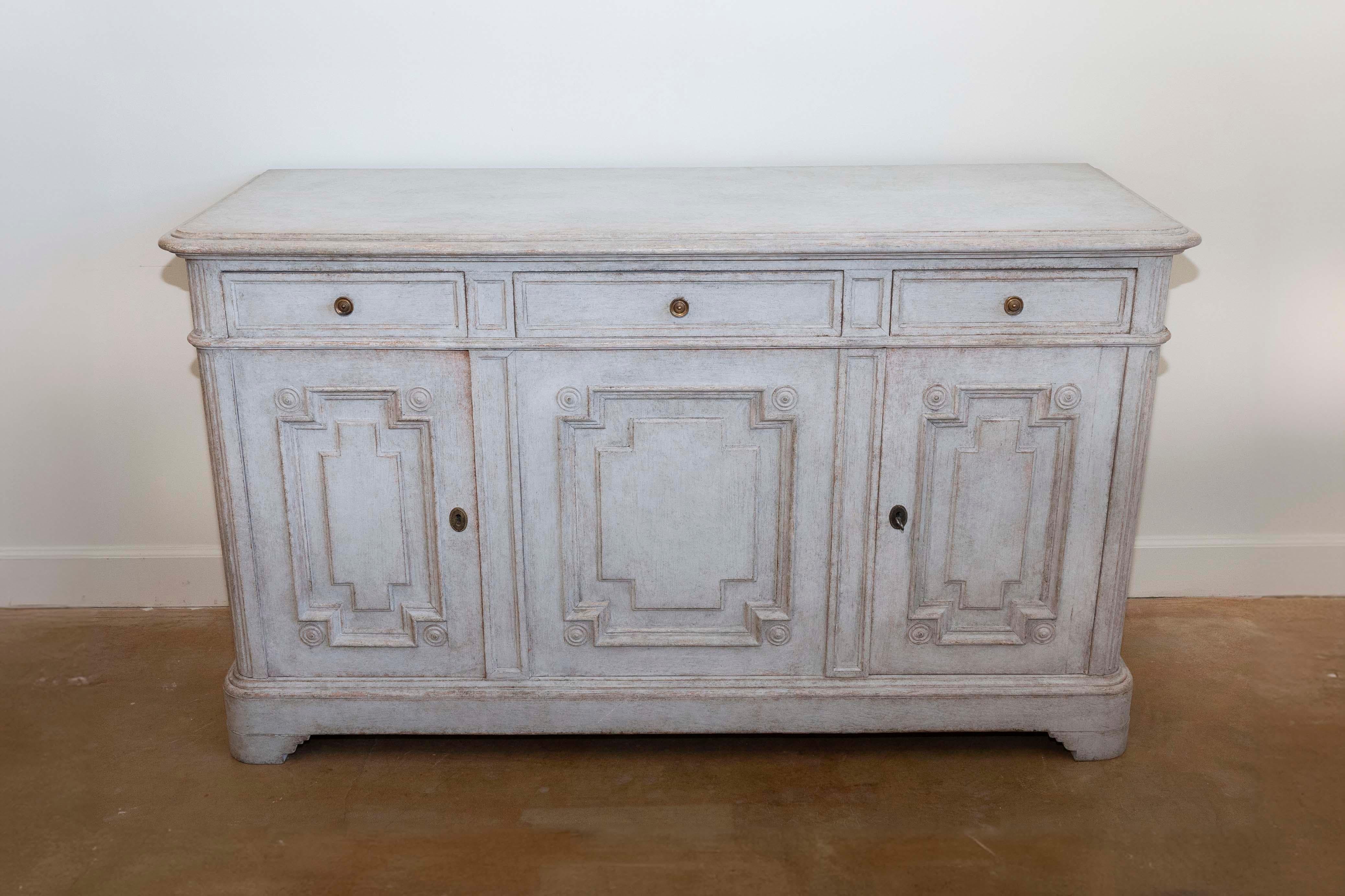 A Swedish Gustavian style painted wood sideboard from circa 1890 with three drawers over three doors, fluted side posts, carved bracket feet and carved geometric motifs. Imbued with the timeless elegance of Swedish Gustavian design, this painted