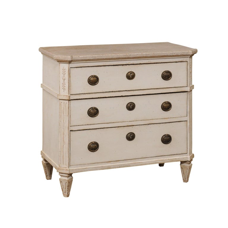A Swedish Gustavian style painted wood chest from late 19th century, with three graduated drawers, Classical hardware, carved foliage and fluted accents. Created in Sweden during the last decade of the 19th century, this Gustavian style chest