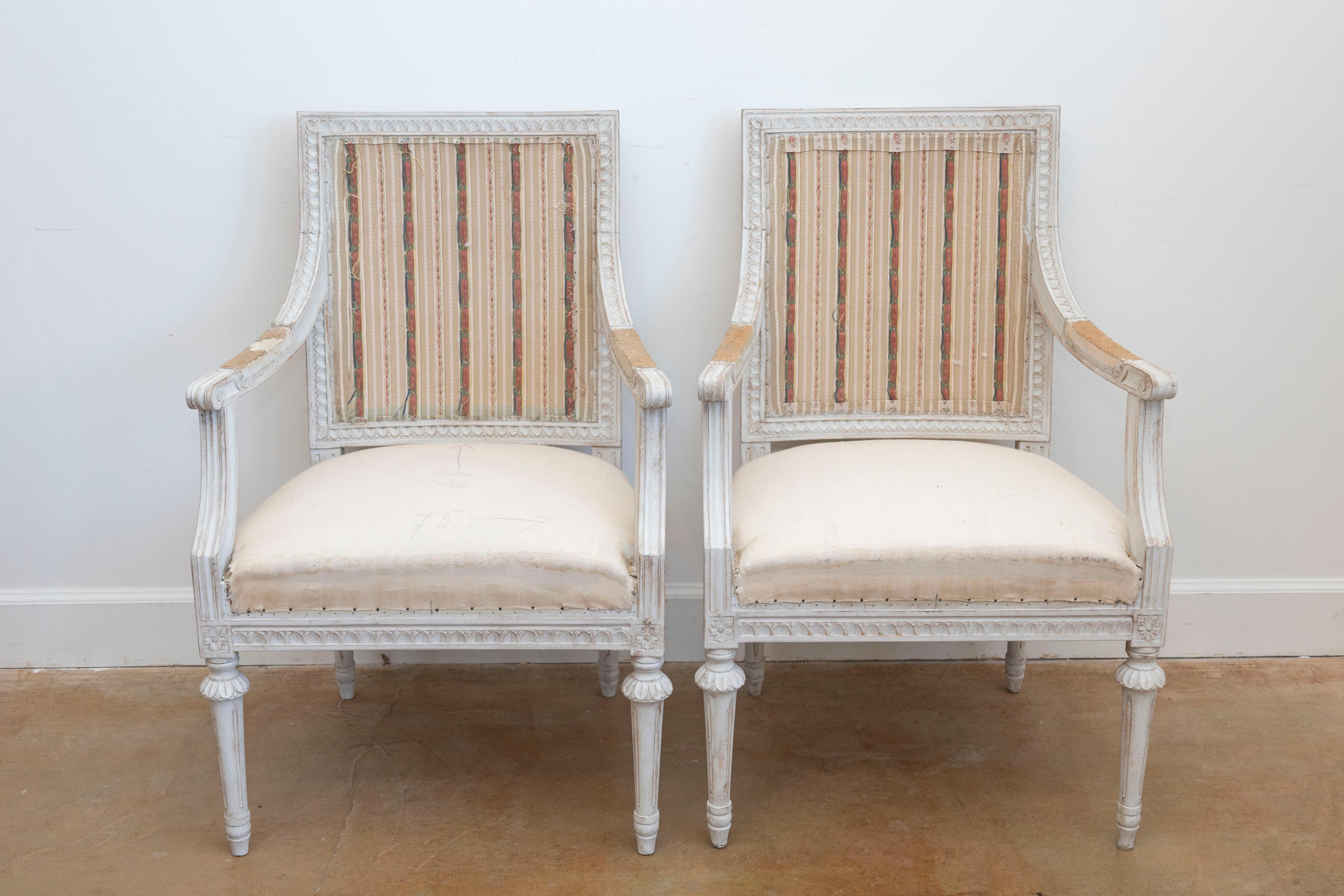 Paire de fauteuils suédois en bois peint de style gustavien du début du 20e siècle, avec des accoudoirs à enroulement, des motifs de feuilles d'eau et de rosettes sculptés et des pieds cannelés. Créée en Suède au début du XXe siècle, cette paire de